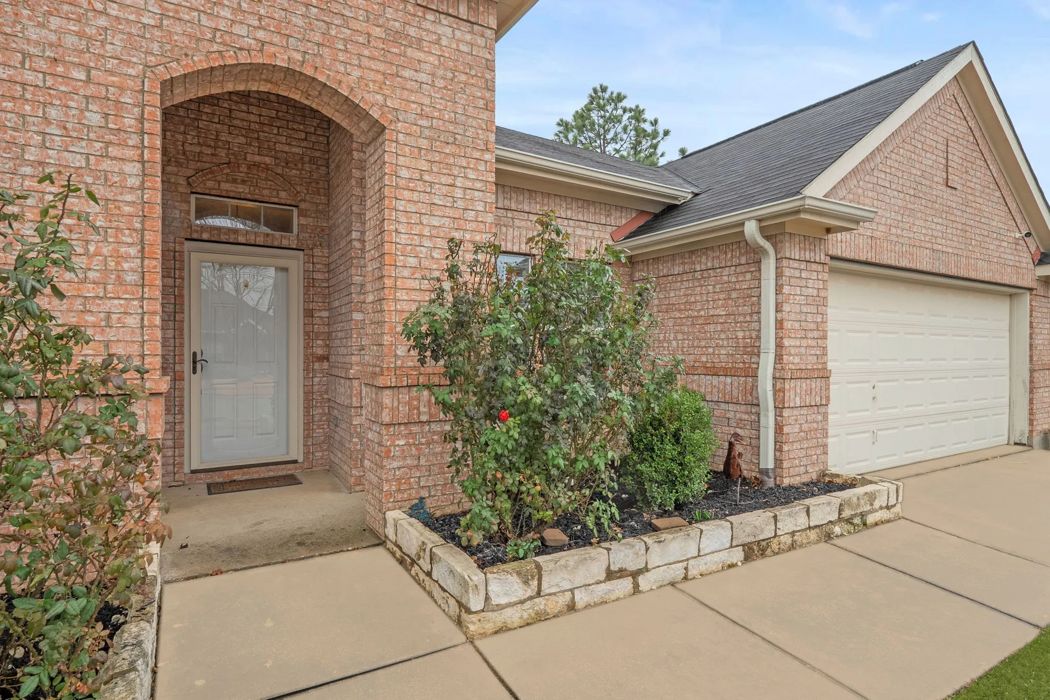 Doorway to property featuring brick siding, roof with shingles, driveway, and a garage