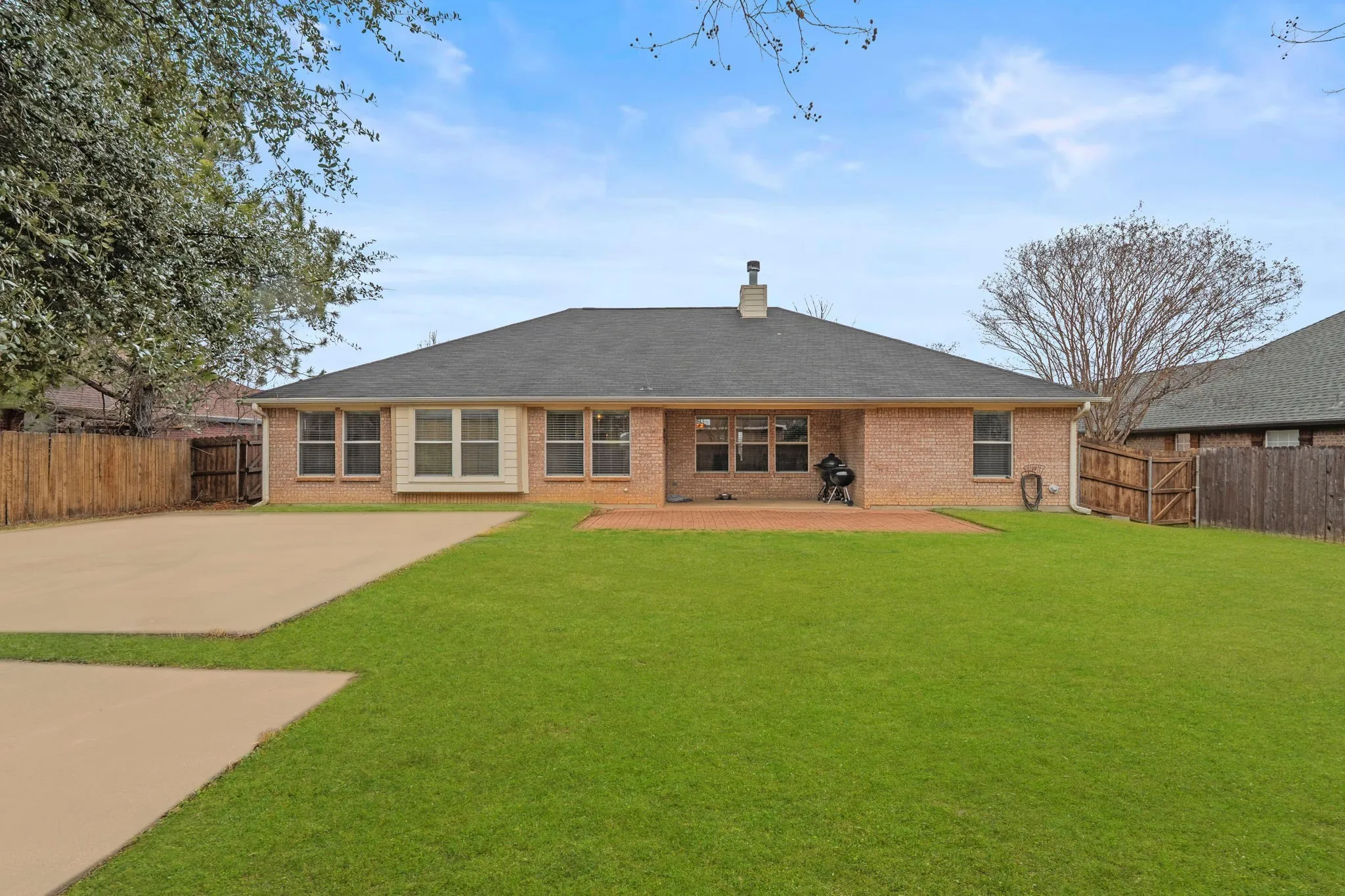 Rear view of house featuring a fenced backyard, brick siding, a chimney, and a patio area