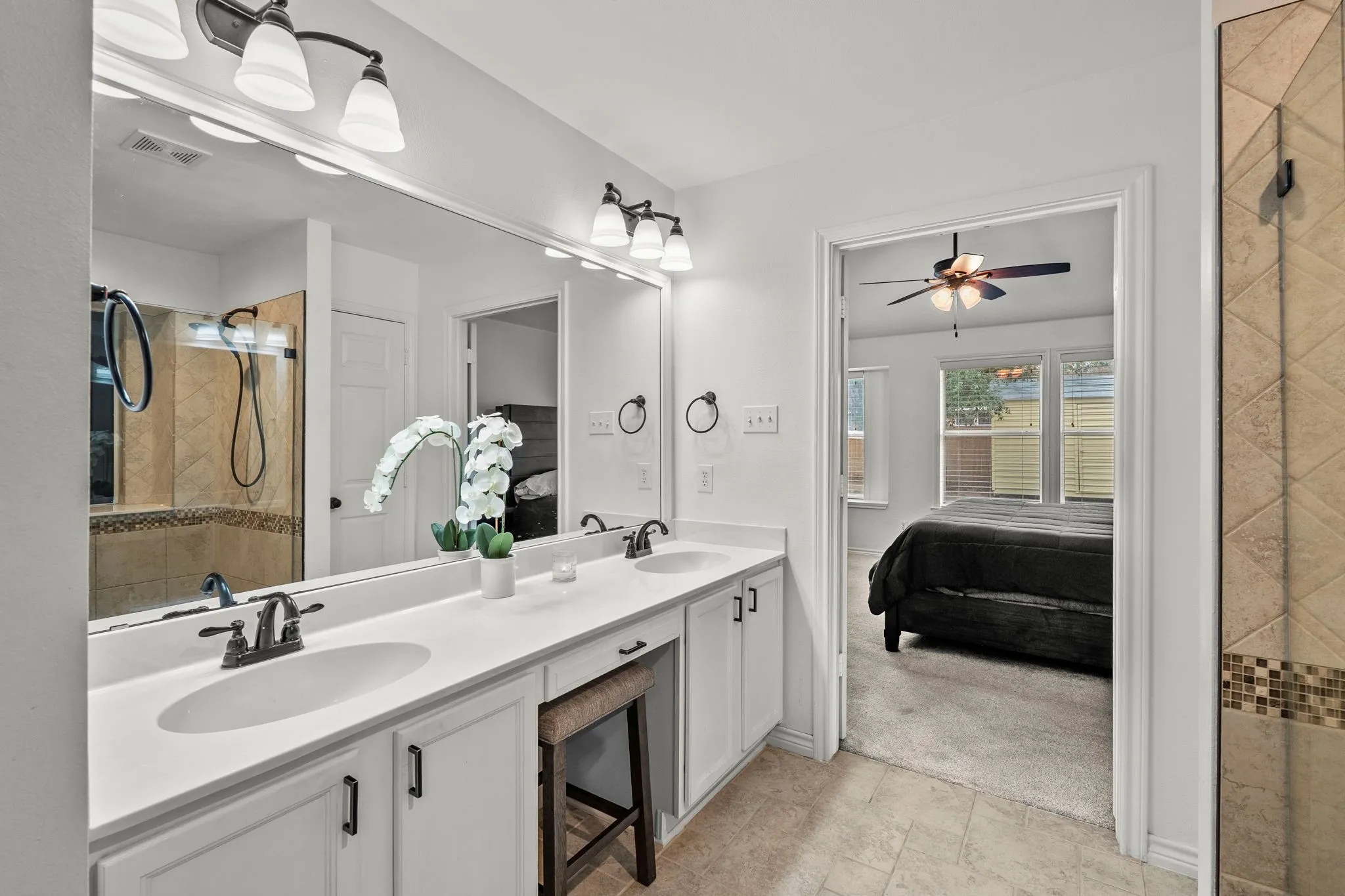 Full bathroom featuring a tile shower, double vanity, ensuite bath, light colored carpet, and a ceiling fan