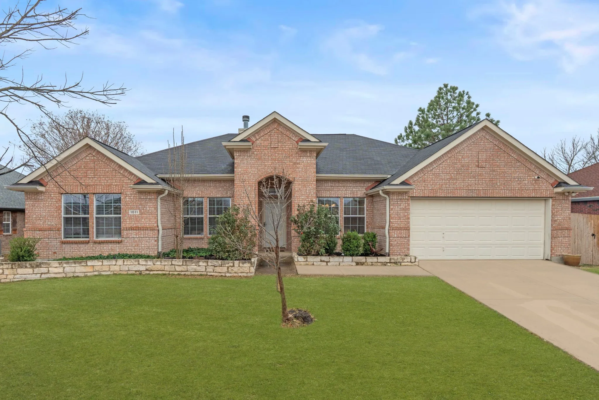 Ranch-style house with a front lawn, brick siding, driveway, roof with shingles, and a garage