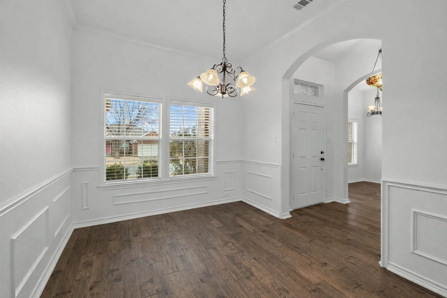 Unfurnished dining area with a chandelier, ornamental molding, dark wood finished floors, healthy amount of natural light, and wainscoting