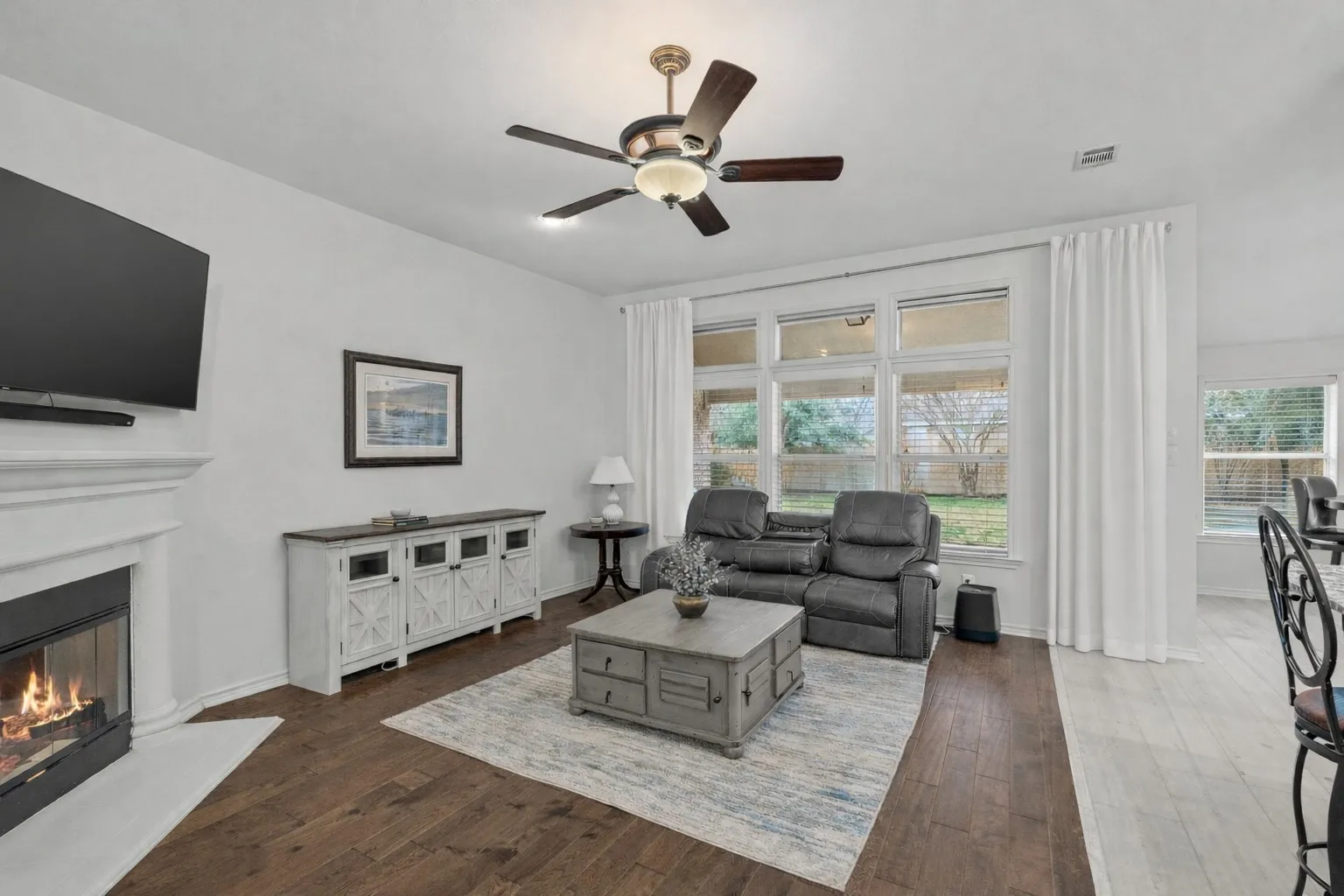 Living area featuring a glass covered fireplace, dark wood-type flooring, ceiling fan, and healthy amount of natural light