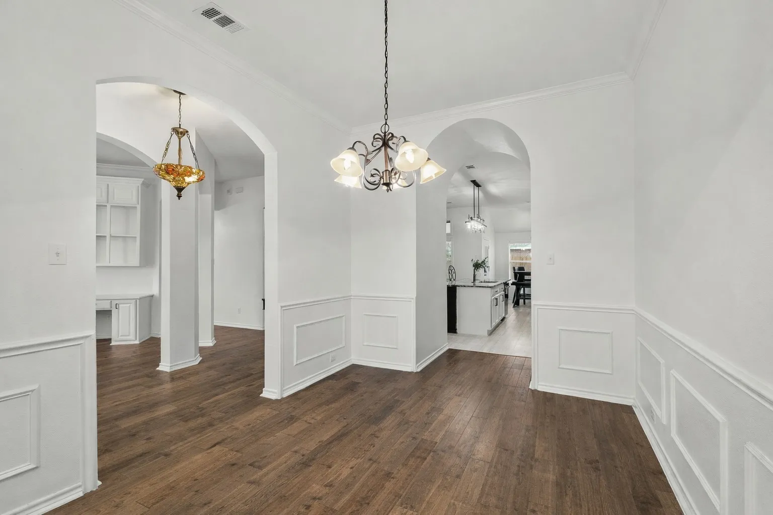 Unfurnished dining area with arched walkways, dark wood-style flooring, a chandelier, wainscoting, and a decorative wall