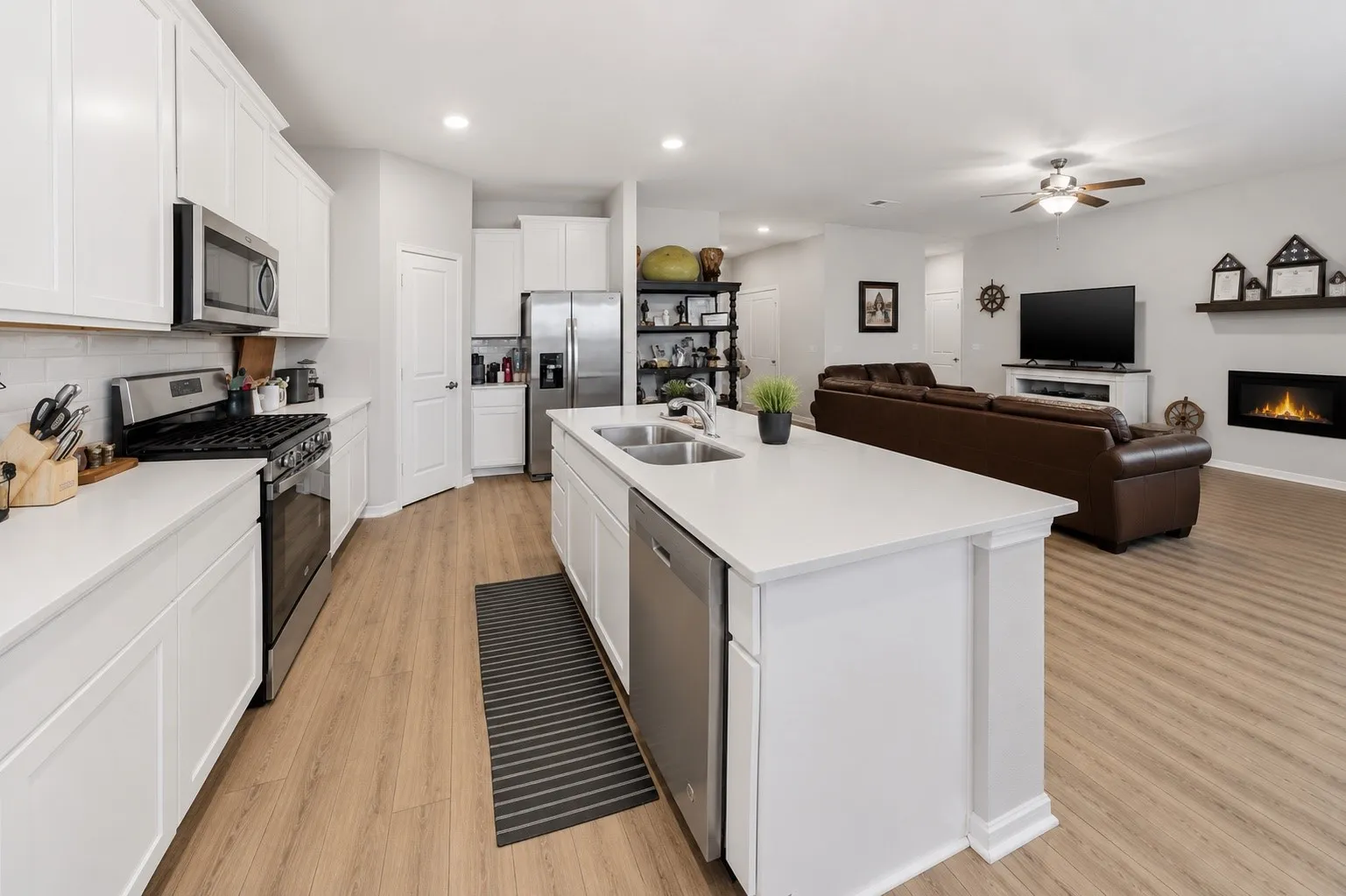 Open-concept space featuring a kitchen with white cabinetry, stainless steel appliances, and a central island with integrated sink