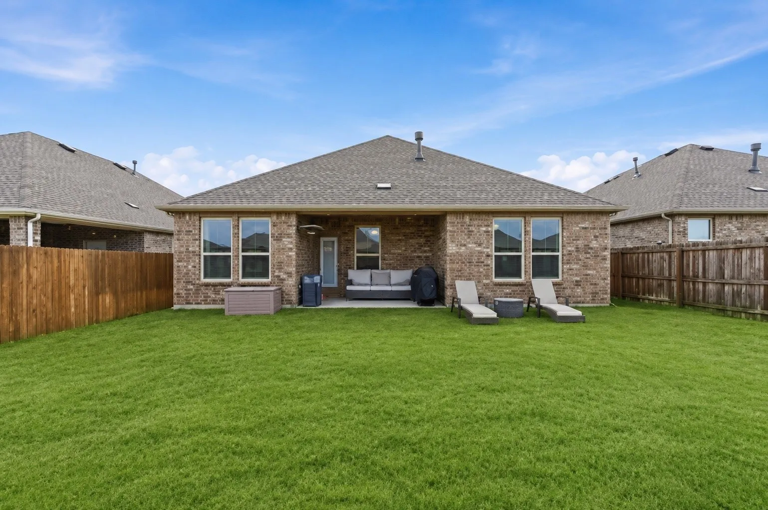 Expansive backyard featuring a manicured lawn, full privacy fencing, and a covered patio with direct access to the interior