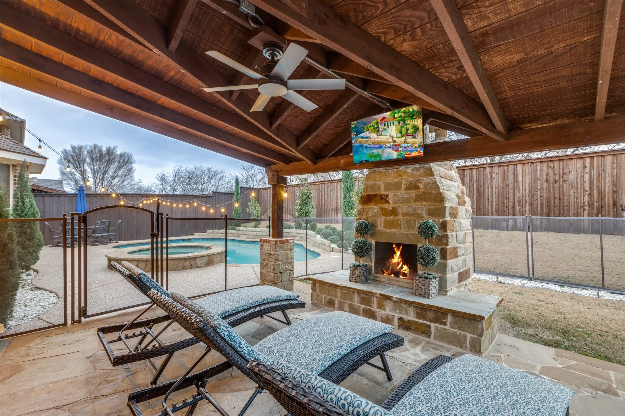 Covered stone patio with stone wood burning fireplace and child fence to pool, spa and grassy yard.