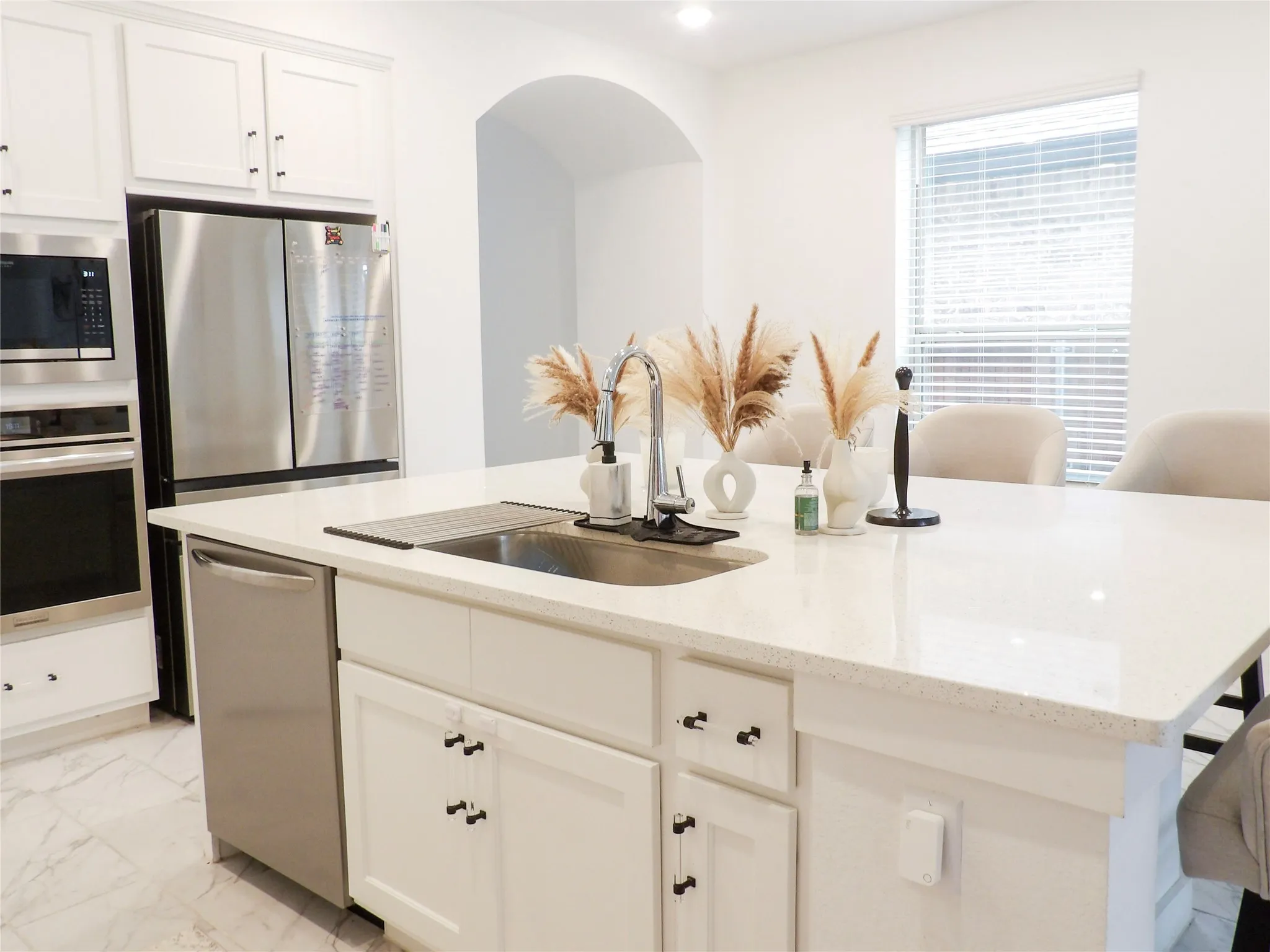 Kitchen featuring white cabinetry, stainless steel appliances, a center island with sink, light stone counters, and light marble finish flooring