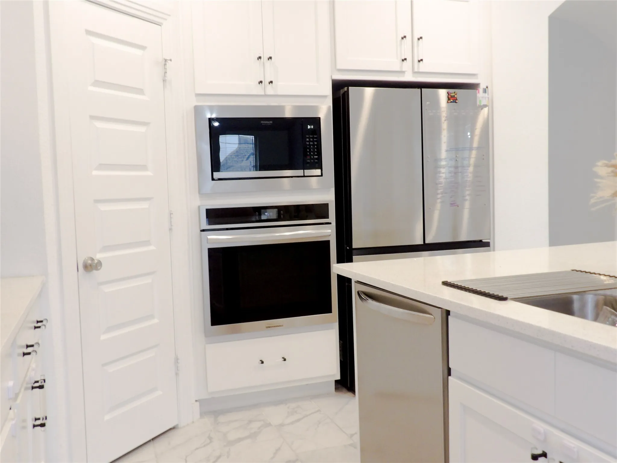 Kitchen with white cabinetry, appliances with stainless steel finishes, light stone countertops, and light marble finish flooring