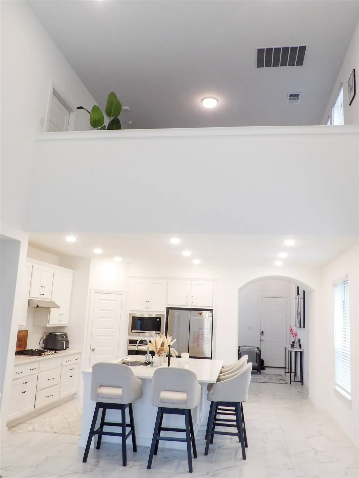Loft view with Kitchen, breakfast bar, white cabinetry, arched walkways, stainless steel appliances, and recessed lighting