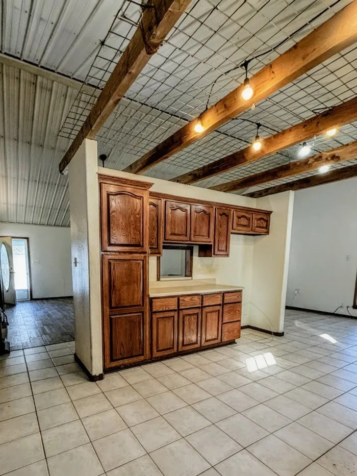 Kitchen with beamed ceiling, light countertops, brown cabinets, and light tile patterned floors