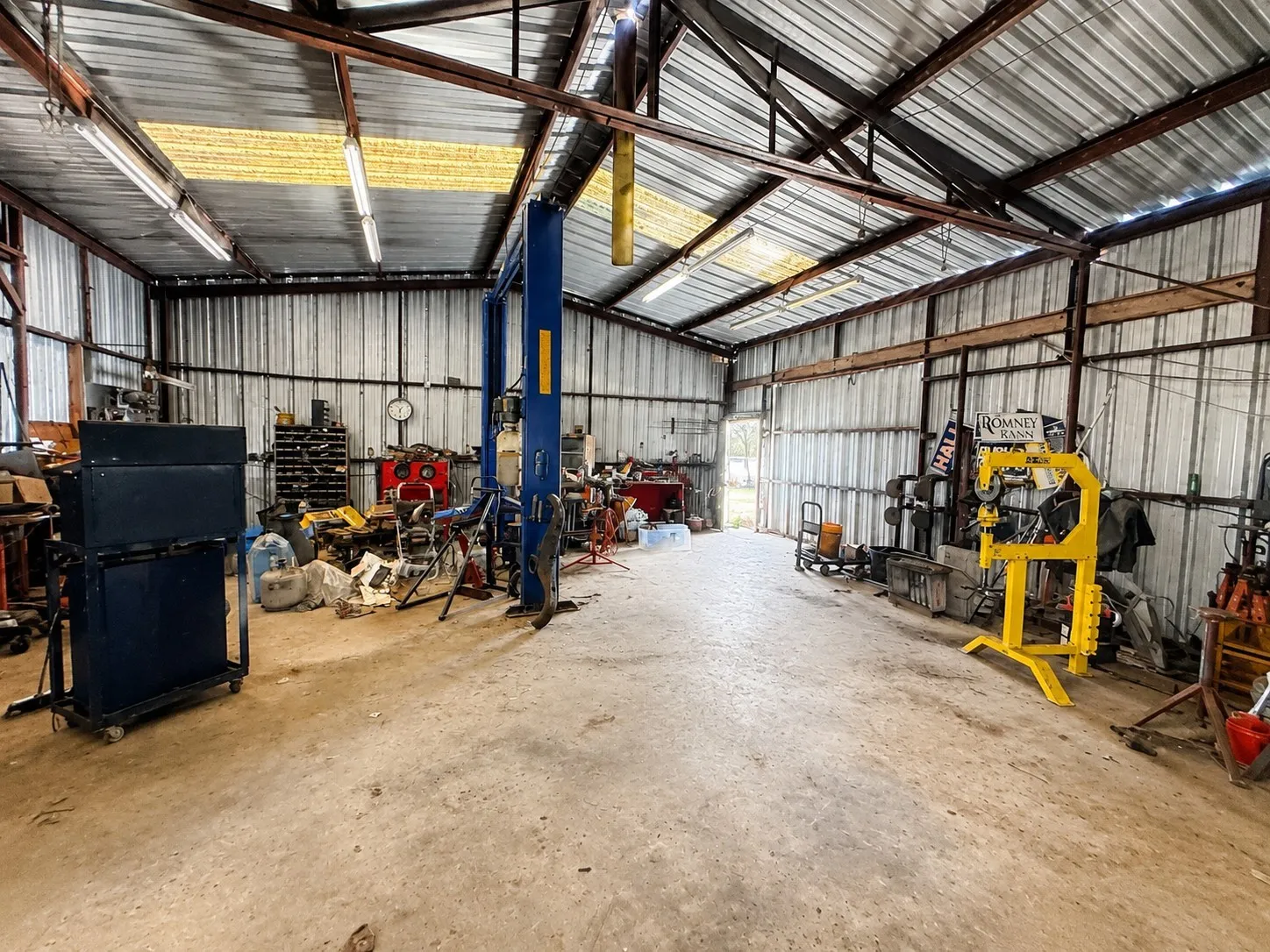 Industrial-style metal building featuring a corrugated metal roof, exposed steel beams, concrete flooring, and an integrated vehicle lift