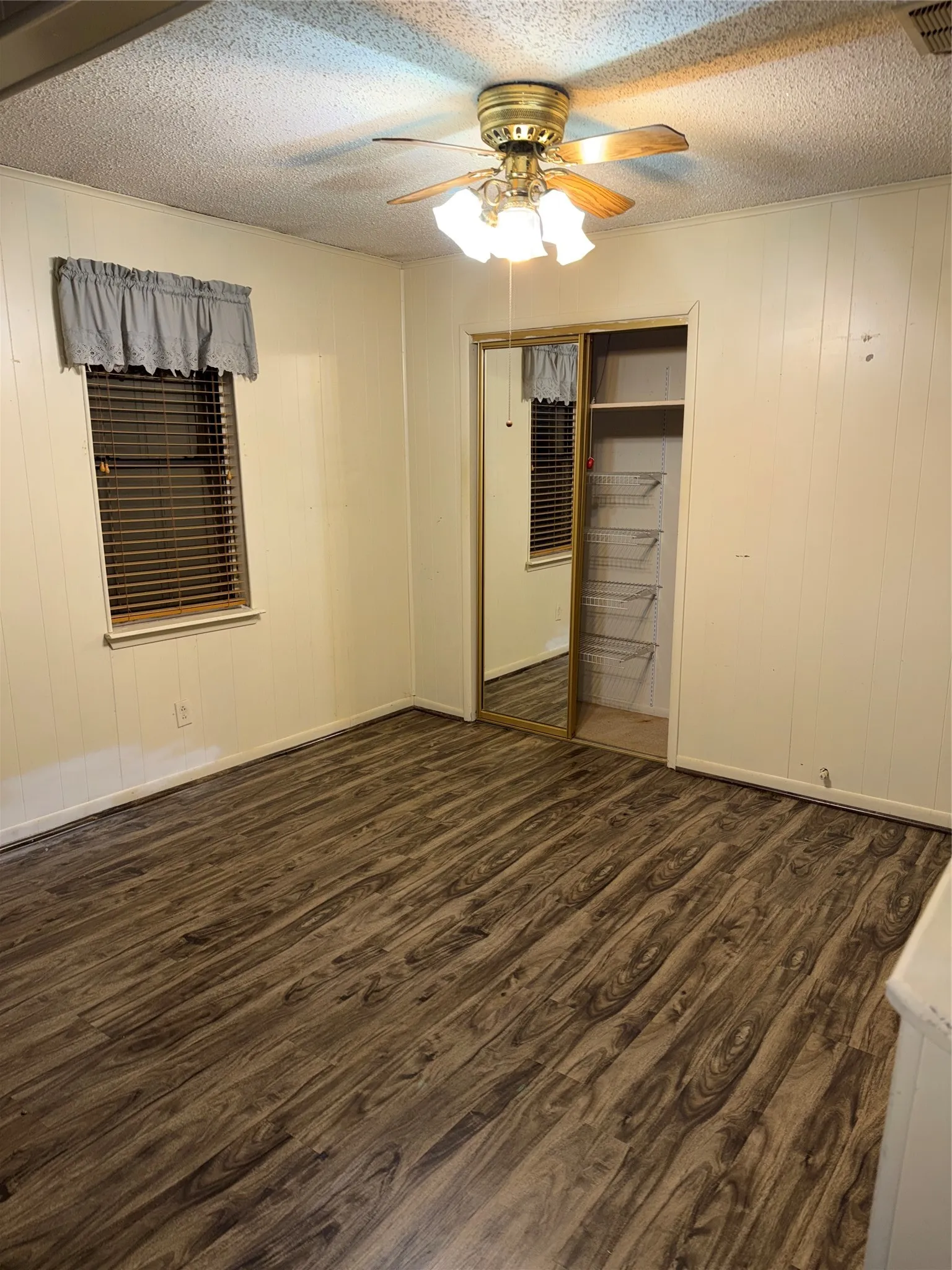 Unfurnished bedroom featuring dark wood-style flooring, a closet, a textured ceiling, ceiling fan, and wooden walls