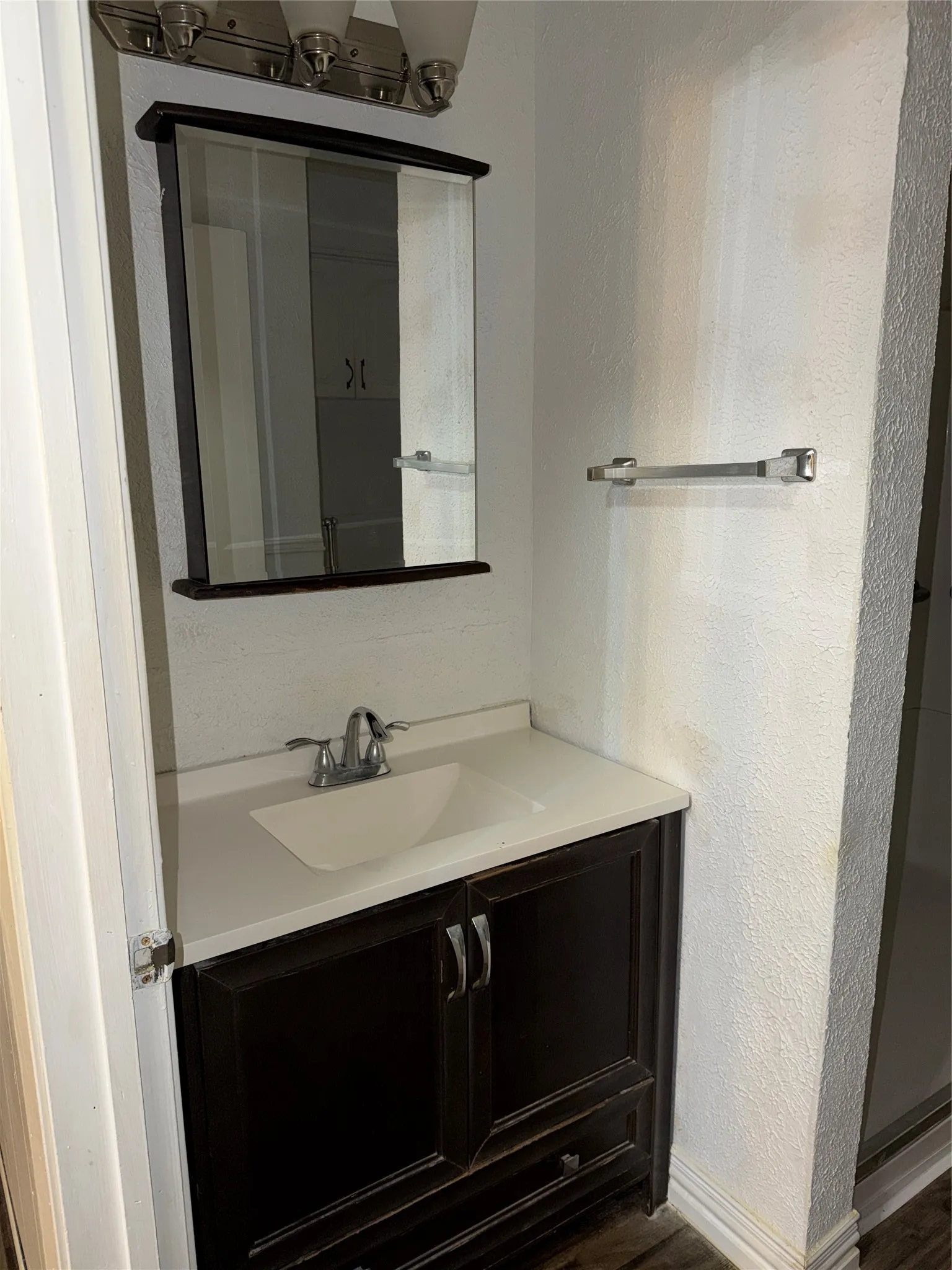 Bathroom with a textured wall, vanity, and dark wood-style flooring
