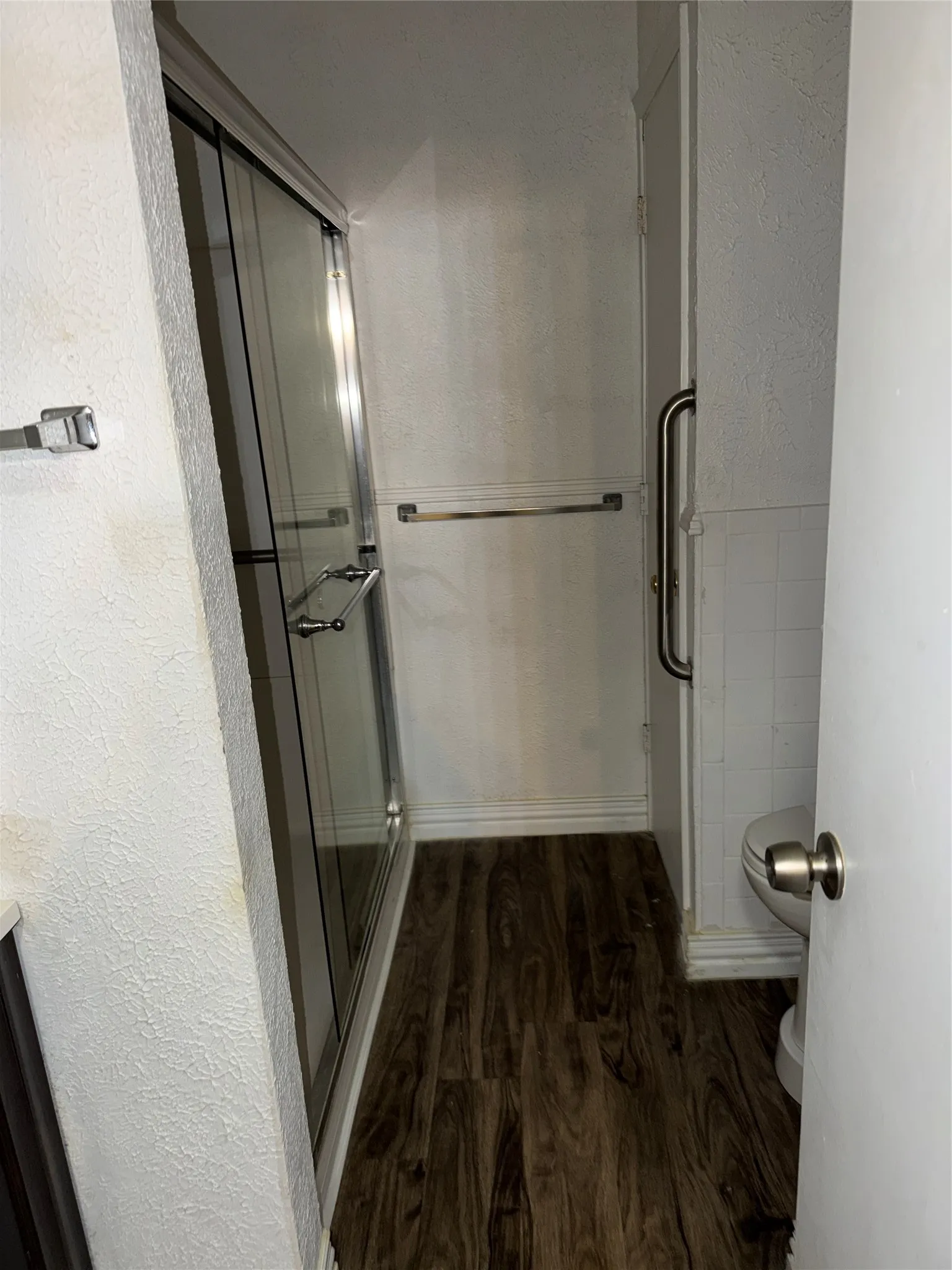 Full bath featuring a textured wall, dark wood finished floors, and a stall shower