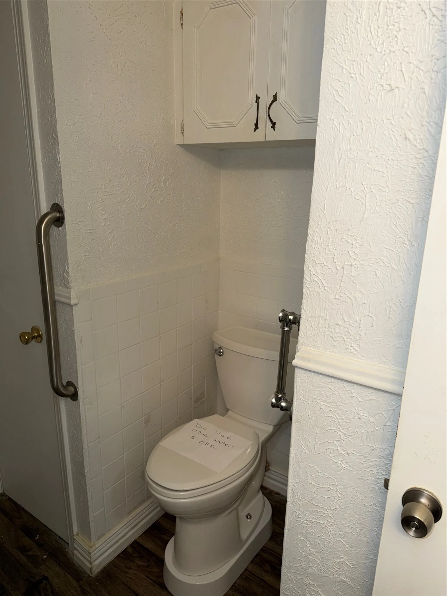 Bathroom featuring a textured wall, dark wood finished floors, wainscoting, and tile walls