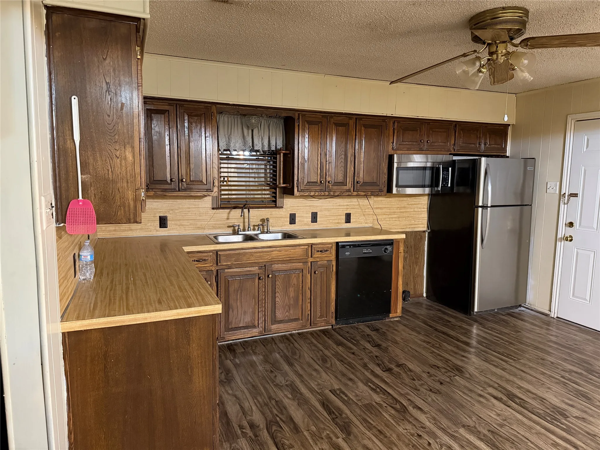 Kitchen with stainless steel appliances, a ceiling fan, light countertops, a textured ceiling, and dark wood finished floors