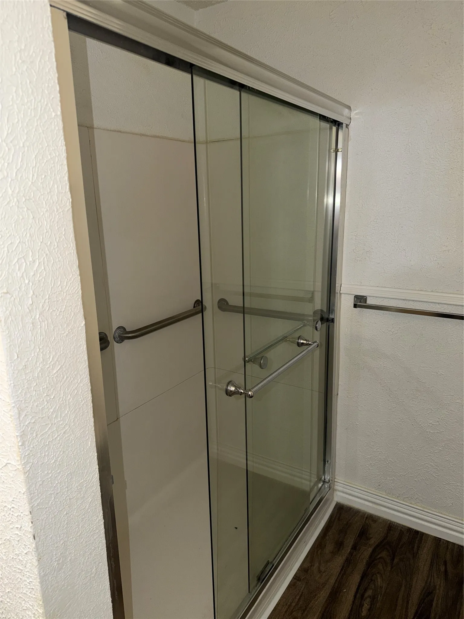 Bathroom with a textured wall, dark wood-style flooring, and a stall shower
