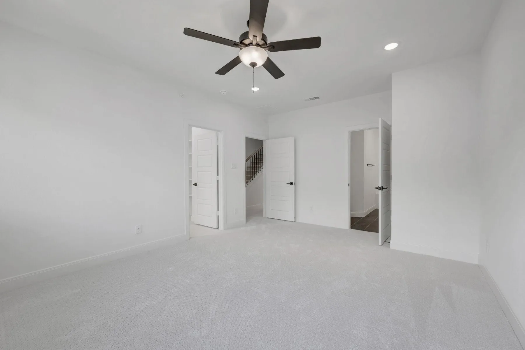 Spacious interior room featuring plush light-toned carpeting, crisp white walls, and a contemporary ceiling fan with integrated lighting