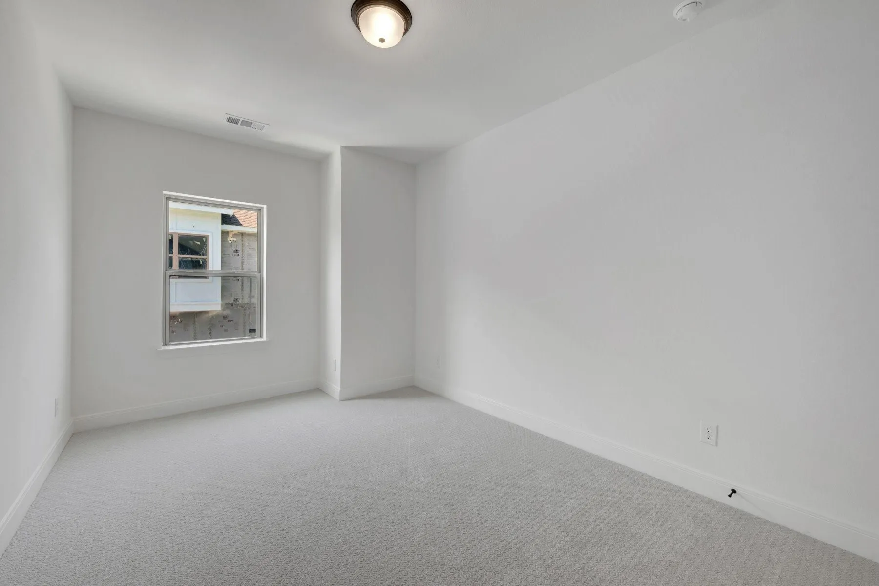Bright room featuring light gray carpeting, white walls, a single window, and a flush-mount ceiling light