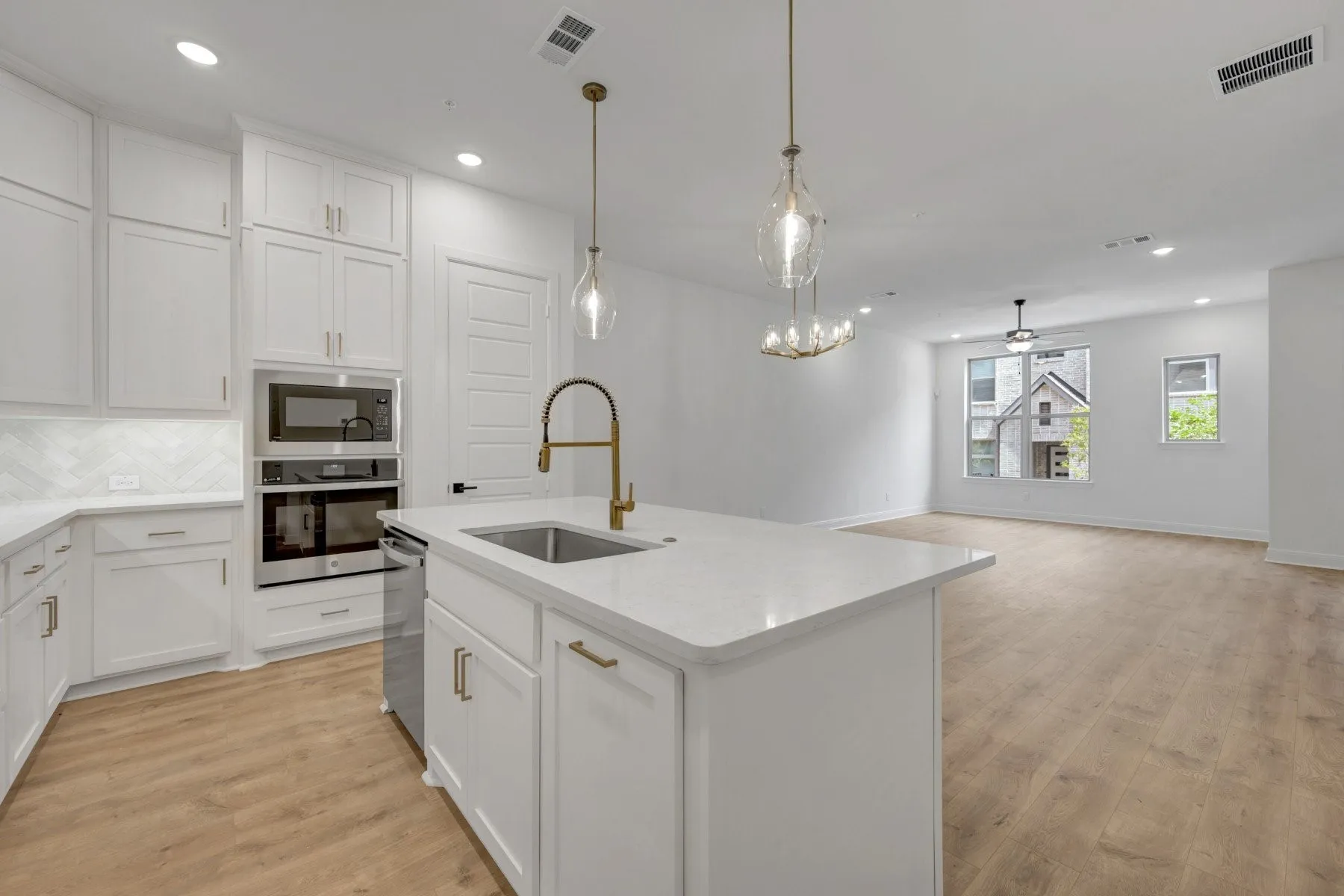 Modern kitchen featuring white cabinetry, quartz countertops, a herringbone tile backsplash, and built-in stainless steel appliances