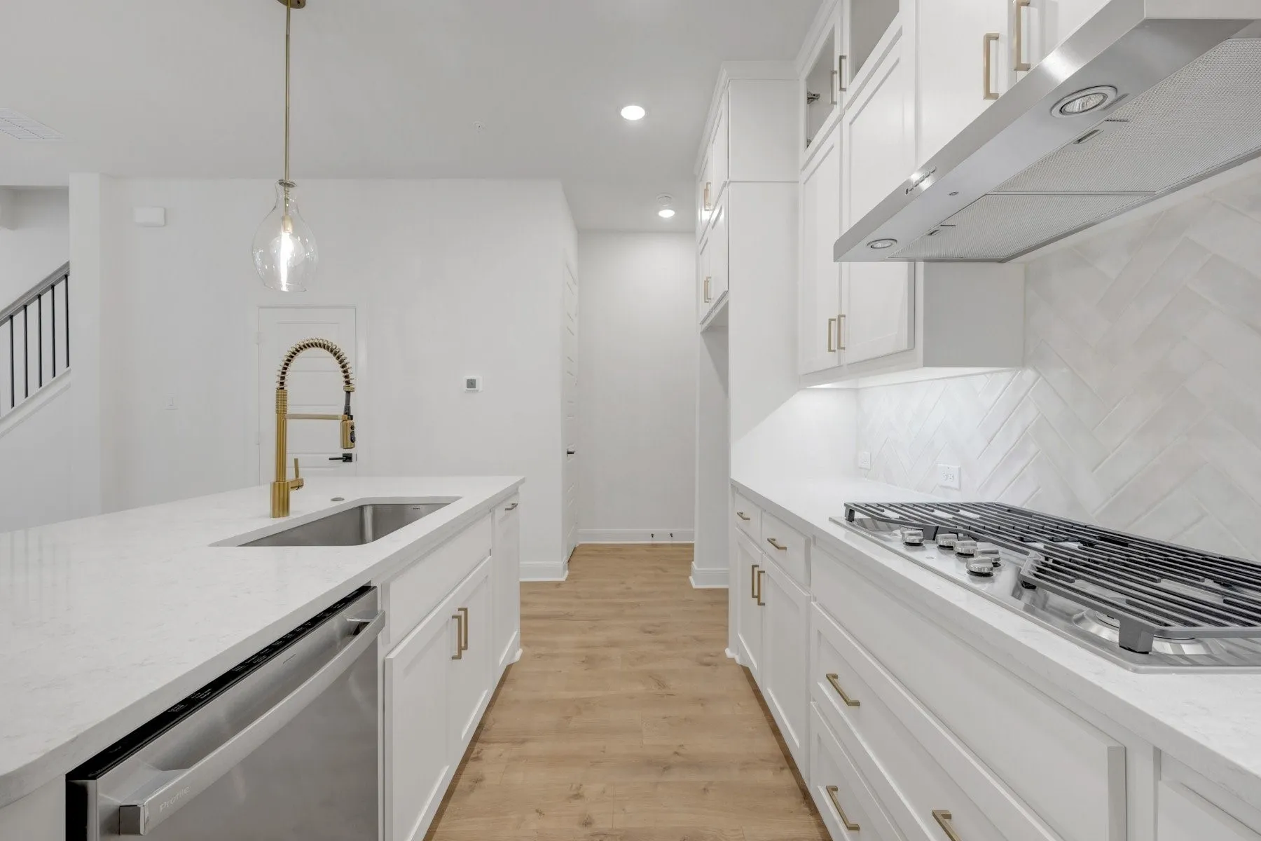 Modern kitchen featuring white cabinetry, light-toned countertops, wood-finish flooring, a stainless steel gas cooktop, and a herringbone tile backsplash