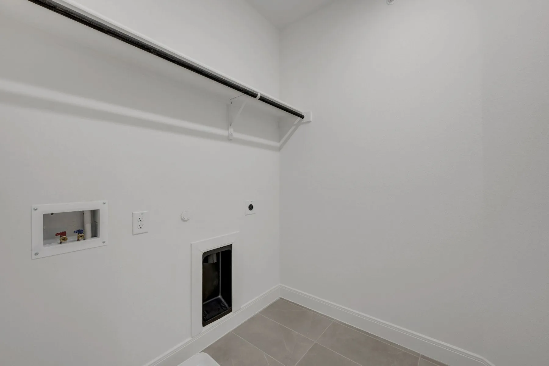 Utility room featuring a clothing rod, wall-mounted shelving support, electrical outlet, and plumbing hookups