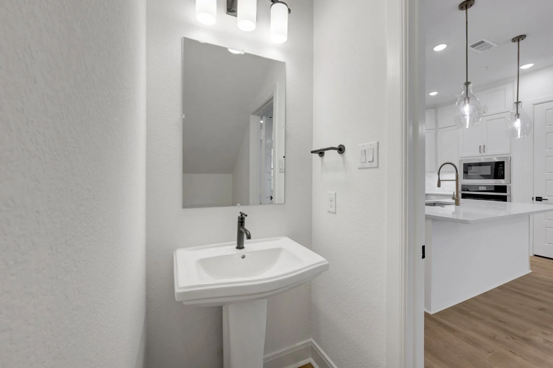 Pedestal sink with dark bronze faucet, framed mirror, and wall-mounted vanity lighting