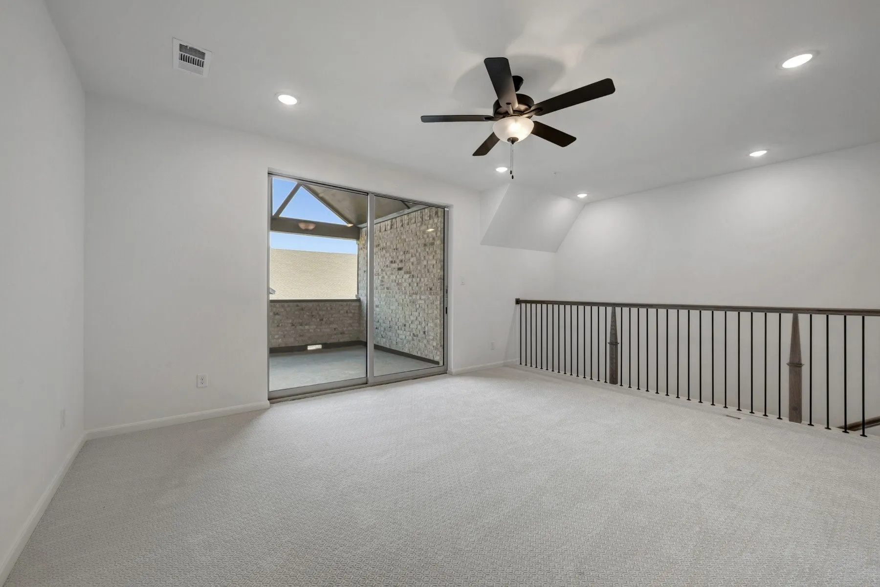 Spacious carpeted room featuring a ceiling fan, recessed lighting, and a dark metal railing