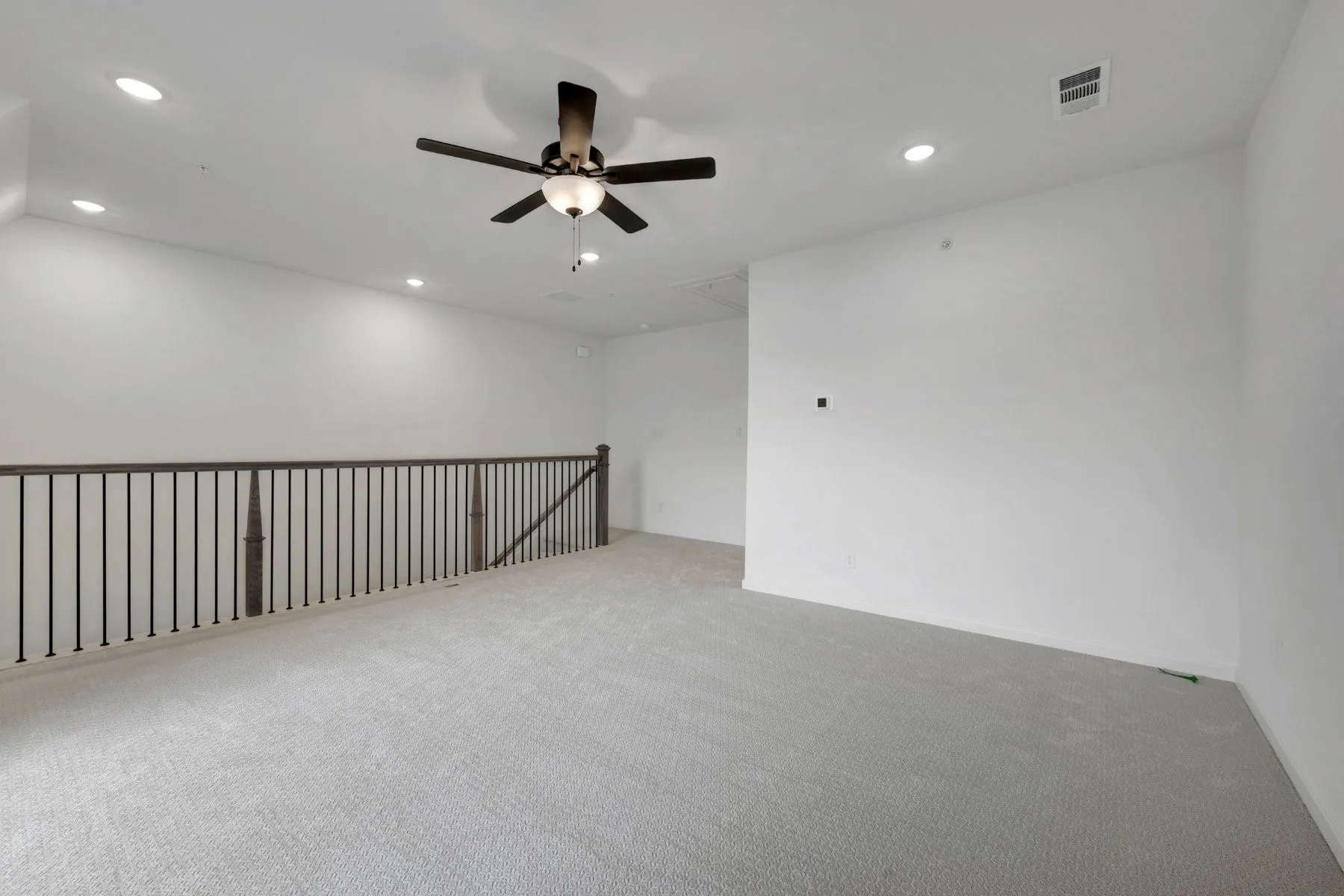 Open loft area featuring recessed lighting, a ceiling fan, light gray carpeting, and a dark wood and wrought iron railing
