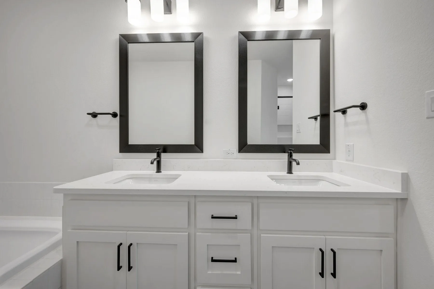Double vanity featuring white cabinetry with matte black hardware, integrated sinks, white countertops, and framed mirrors with overhead lighting