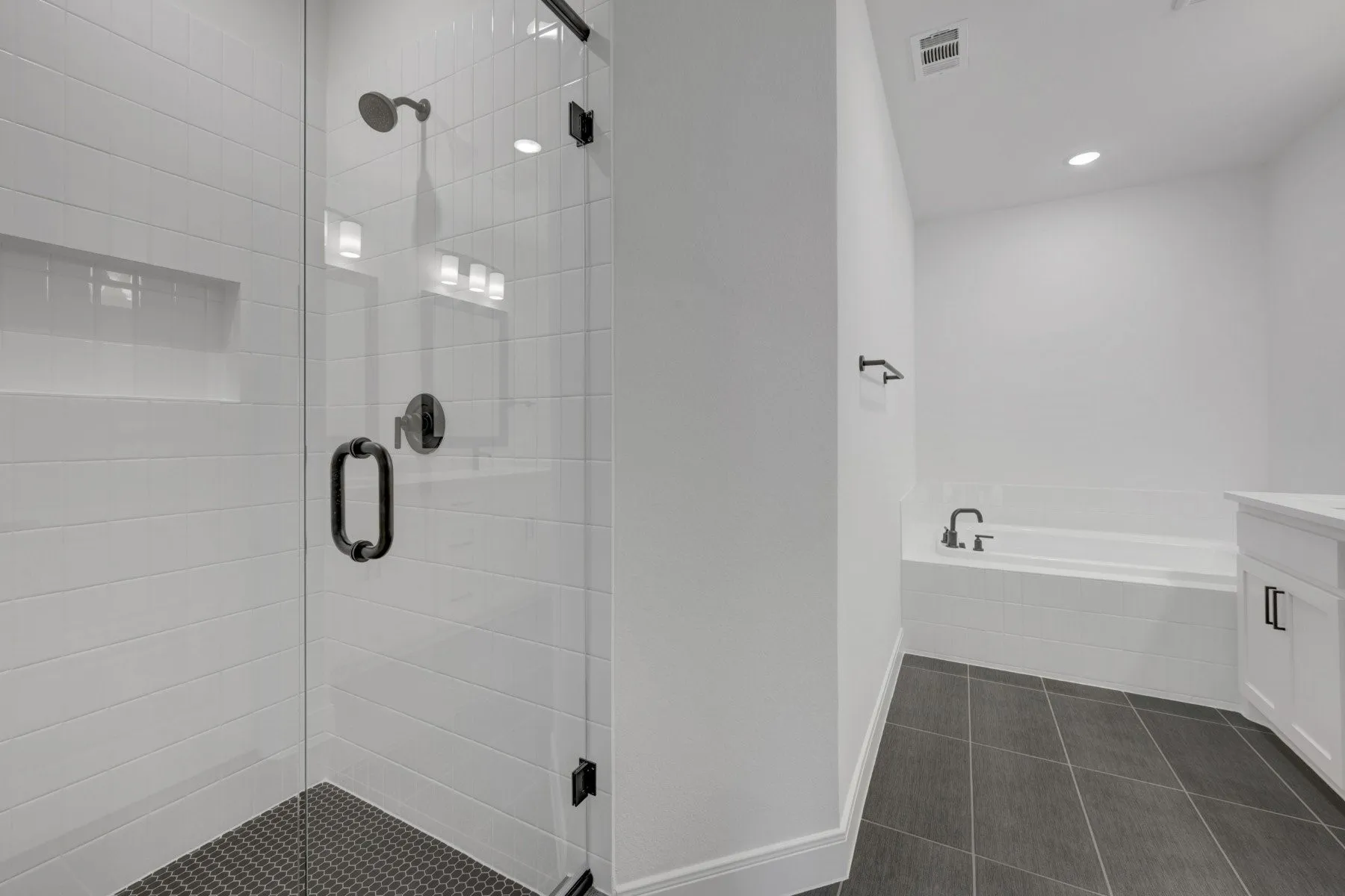 Spacious bathroom featuring a glass-enclosed shower with subway tile surround and dark penny tile flooring, a built-in bathtub with subway tile apron, dark tile flooring, and a white vanity with dark hardware