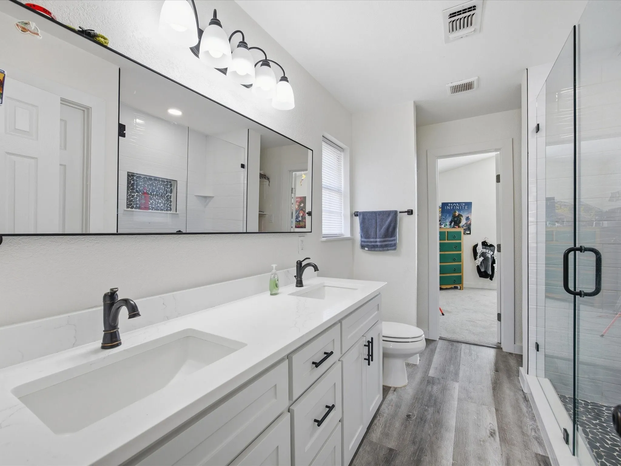 Full bath with double vanity, a stall shower, and light wood-style flooring