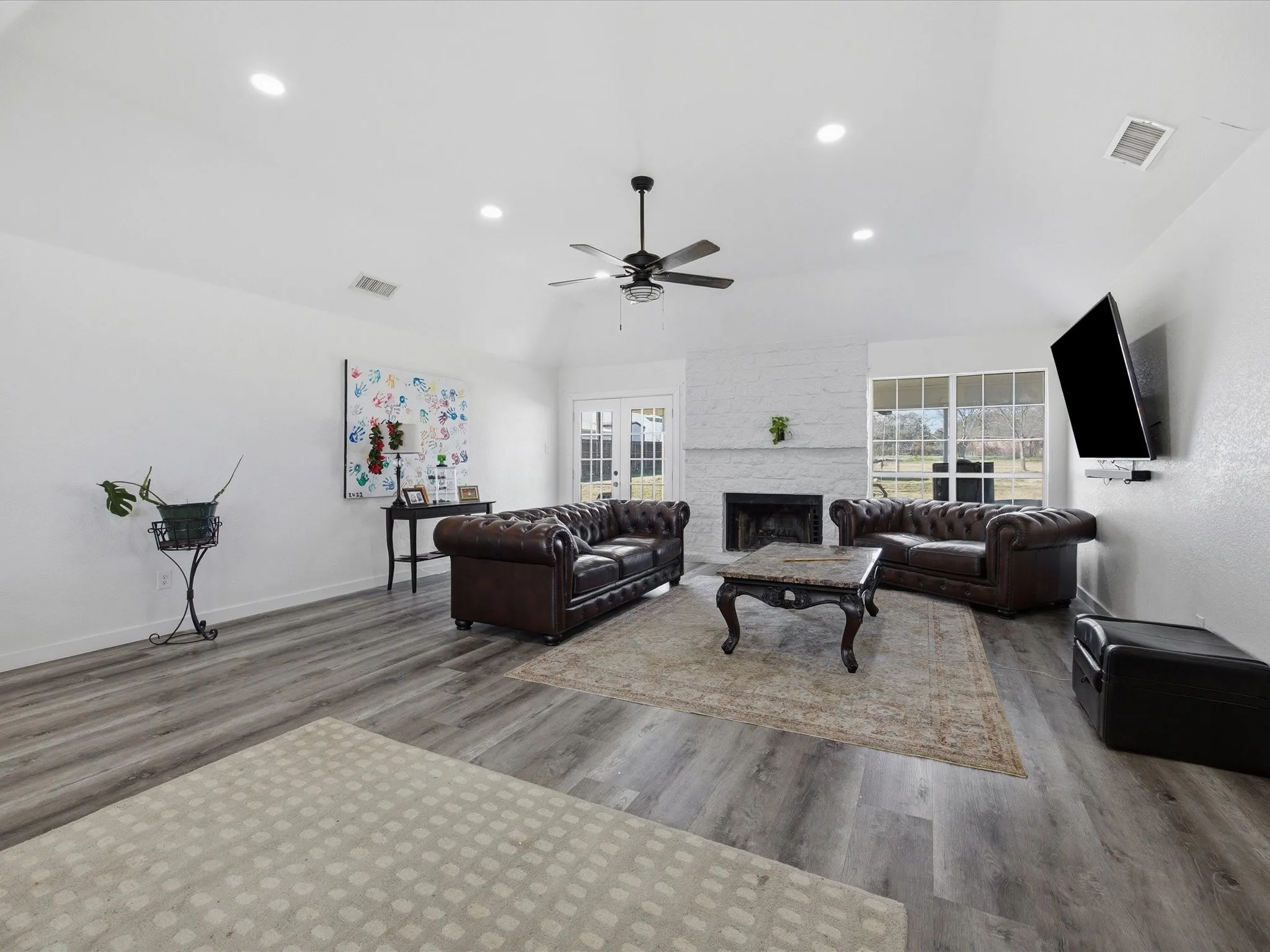 Living room with light wood-style floors, lofted ceiling, a stone fireplace, a ceiling fan, and recessed lighting