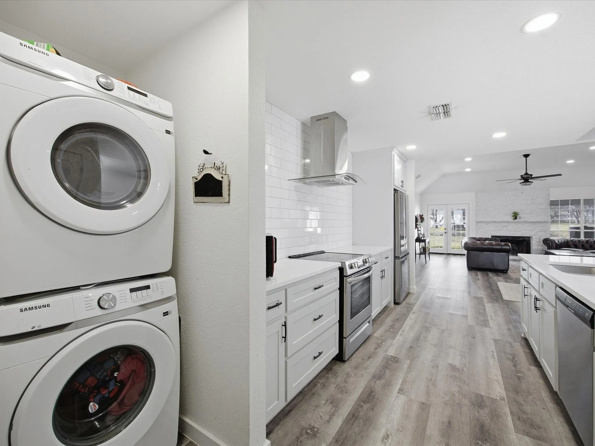 Laundry area featuring light wood-style floors, estacked washer and dryer, a fireplace, recessed lighting, and a ceiling fan