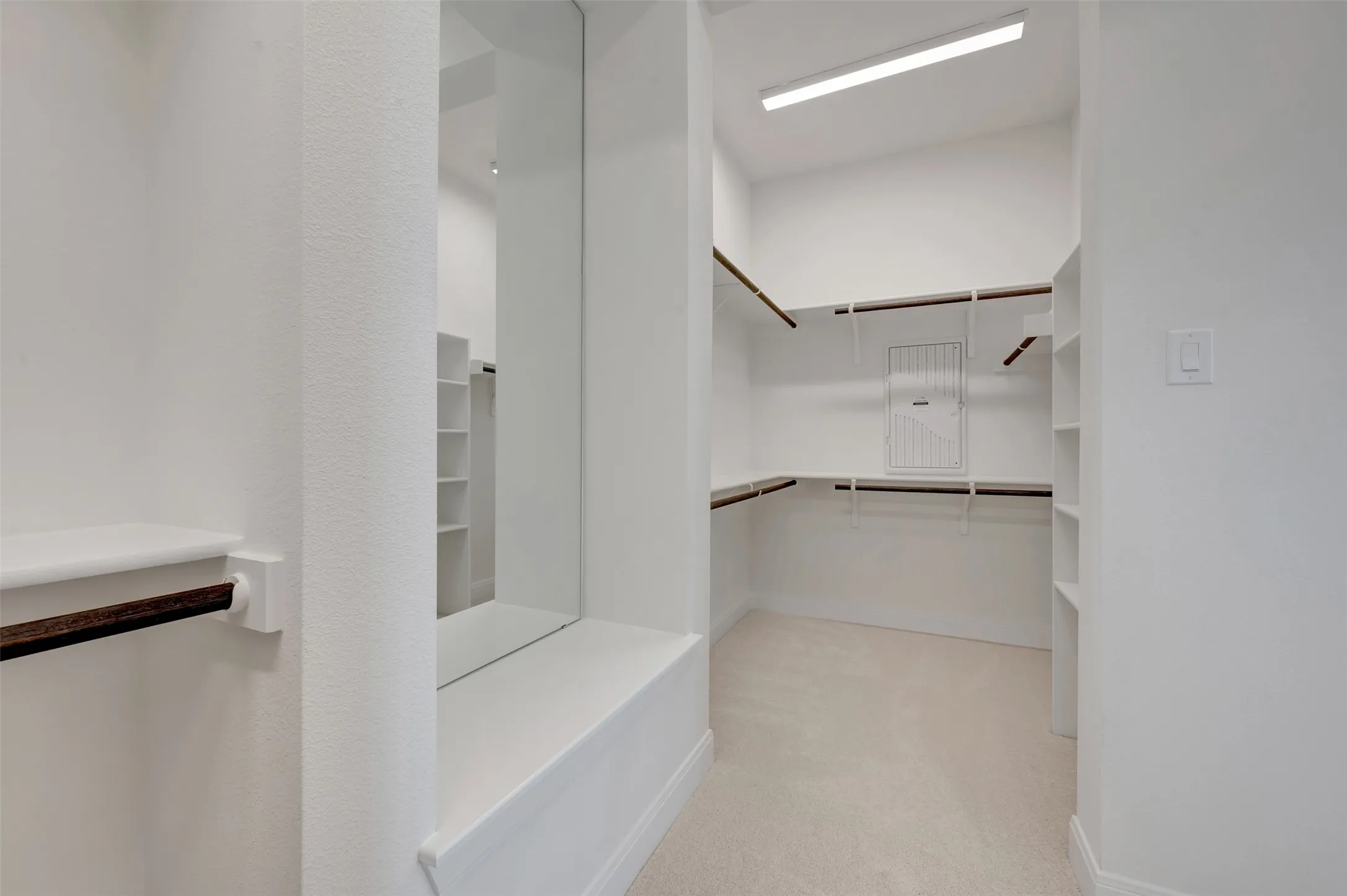 Spacious walk-in closet featuring white built-in shelving, wood-finish hanging rods, and carpeting