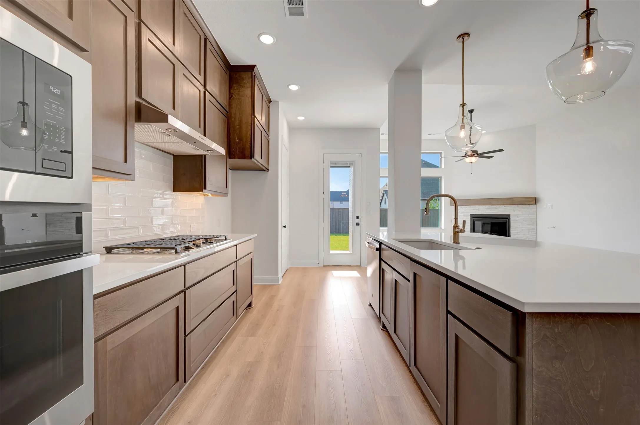 Modern kitchen featuring wood-finish cabinetry, white subway tile backsplash, and stainless steel appliances including a built-in oven and microwave