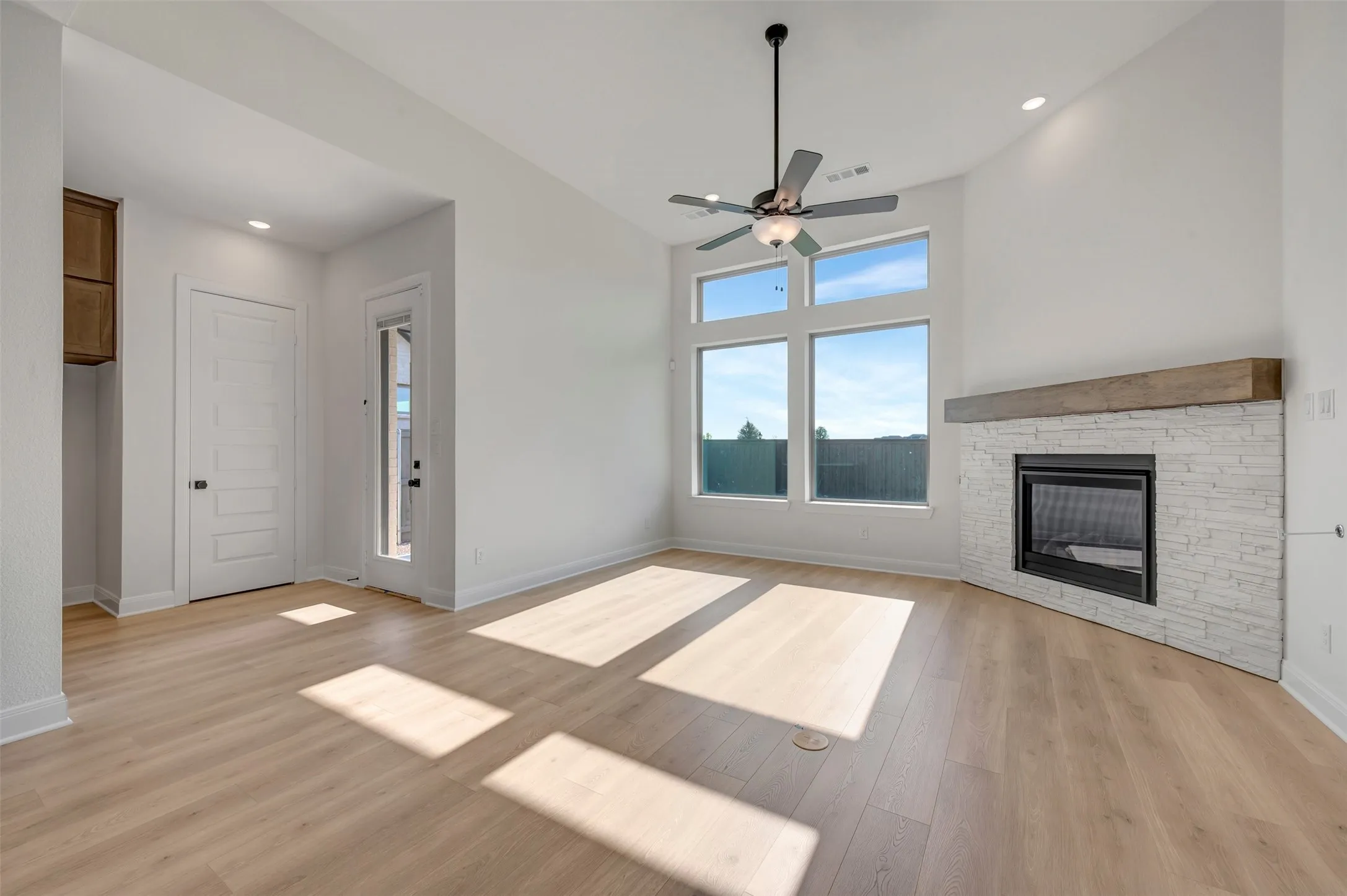 Living area featuring wood-finish flooring and a corner fireplace with a white stacked stone surround and wood mantel