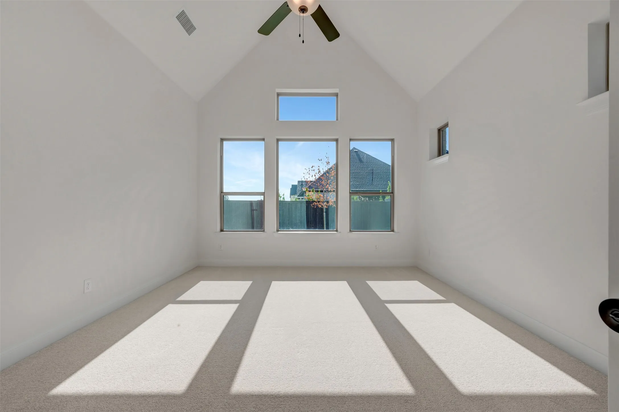 Vaulted ceiling room featuring a ceiling fan, three large windows, an additional transom window, and neutral-toned carpeting