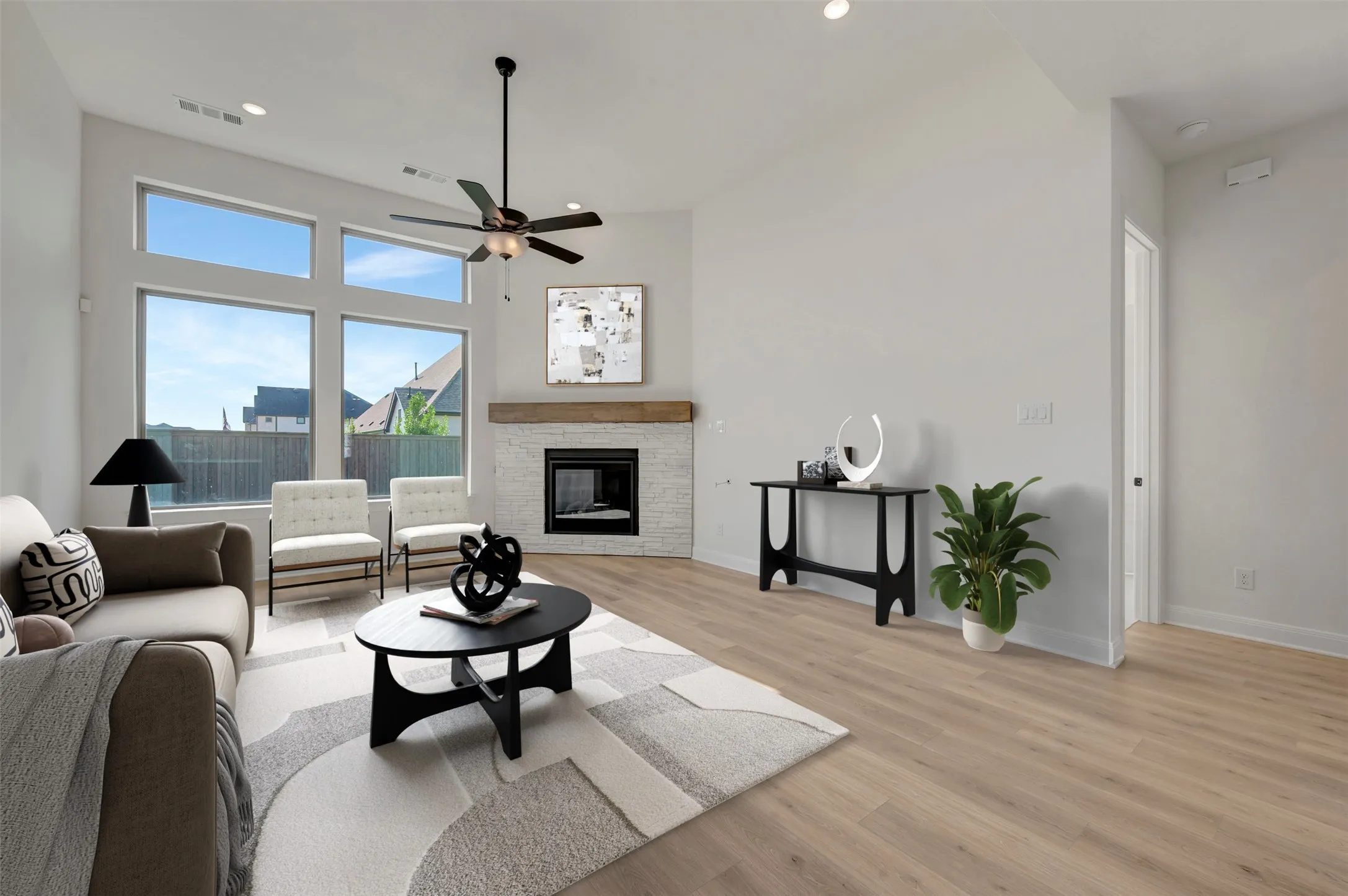 Vaulted ceilings showcasing multiple large windows, wood-finish flooring, a ceiling fan with integrated lighting, and a fireplace with a white brick surround and wood mantel