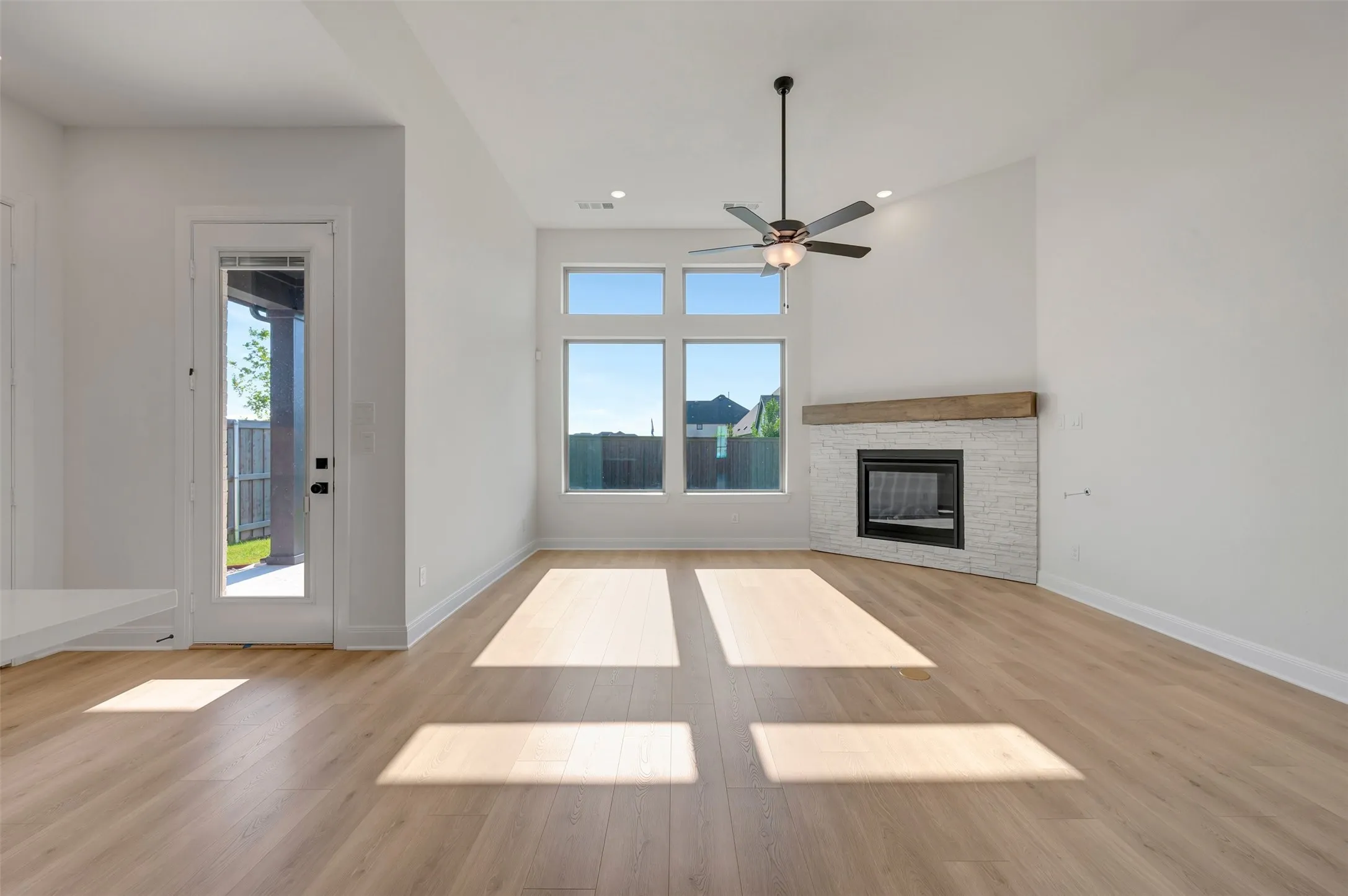Spacious living area featuring wood-finish flooring, a contemporary fireplace with a stone surround and wood mantel, and multiple​​‌​​​​‌​​‌‌​‌‌​​​‌‌​‌​‌​‌​​​‌​​ windows
