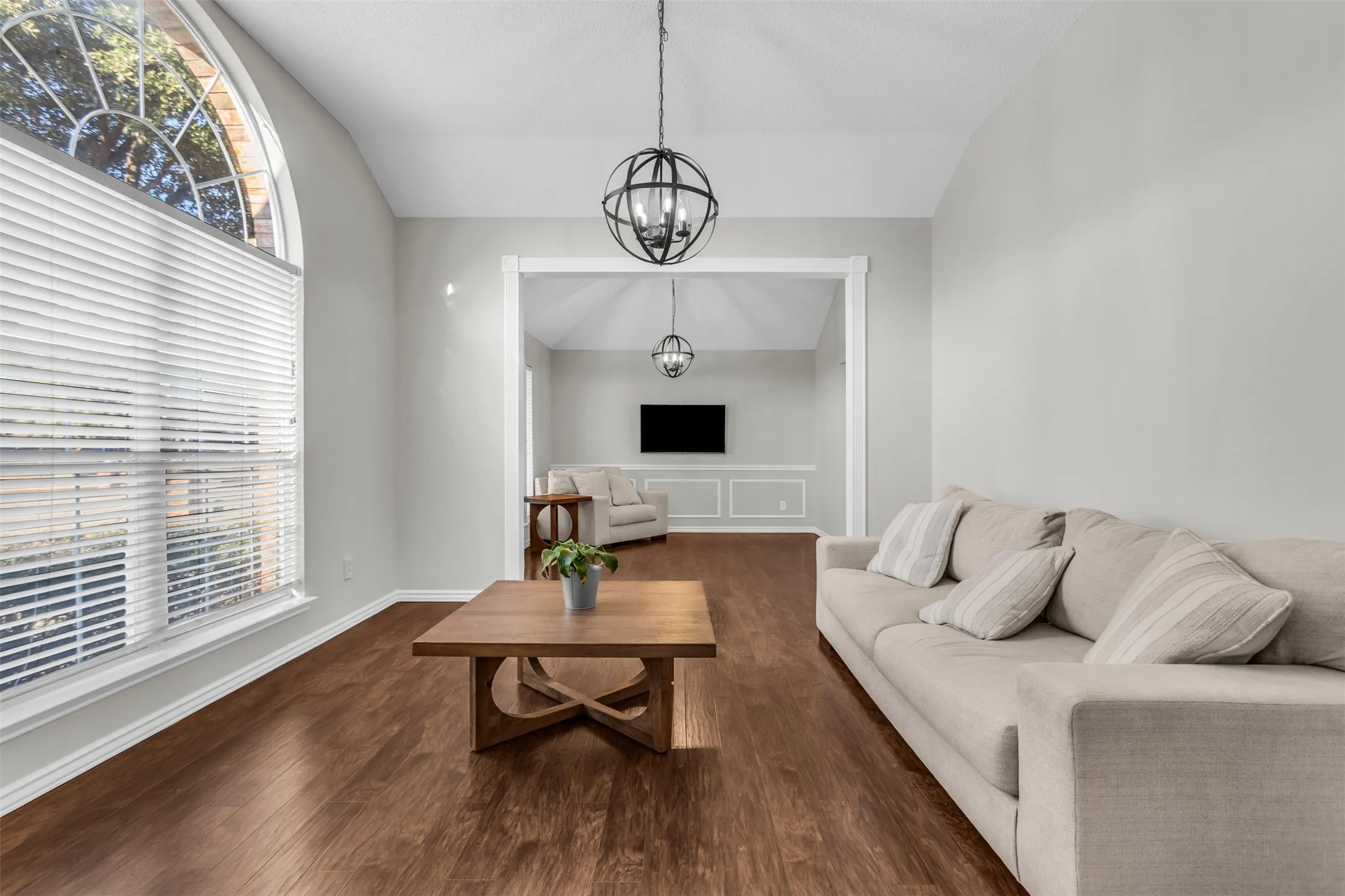 Versatile formal living area boasting tall arched windows, custom lighting, and beautiful hardwood floors.