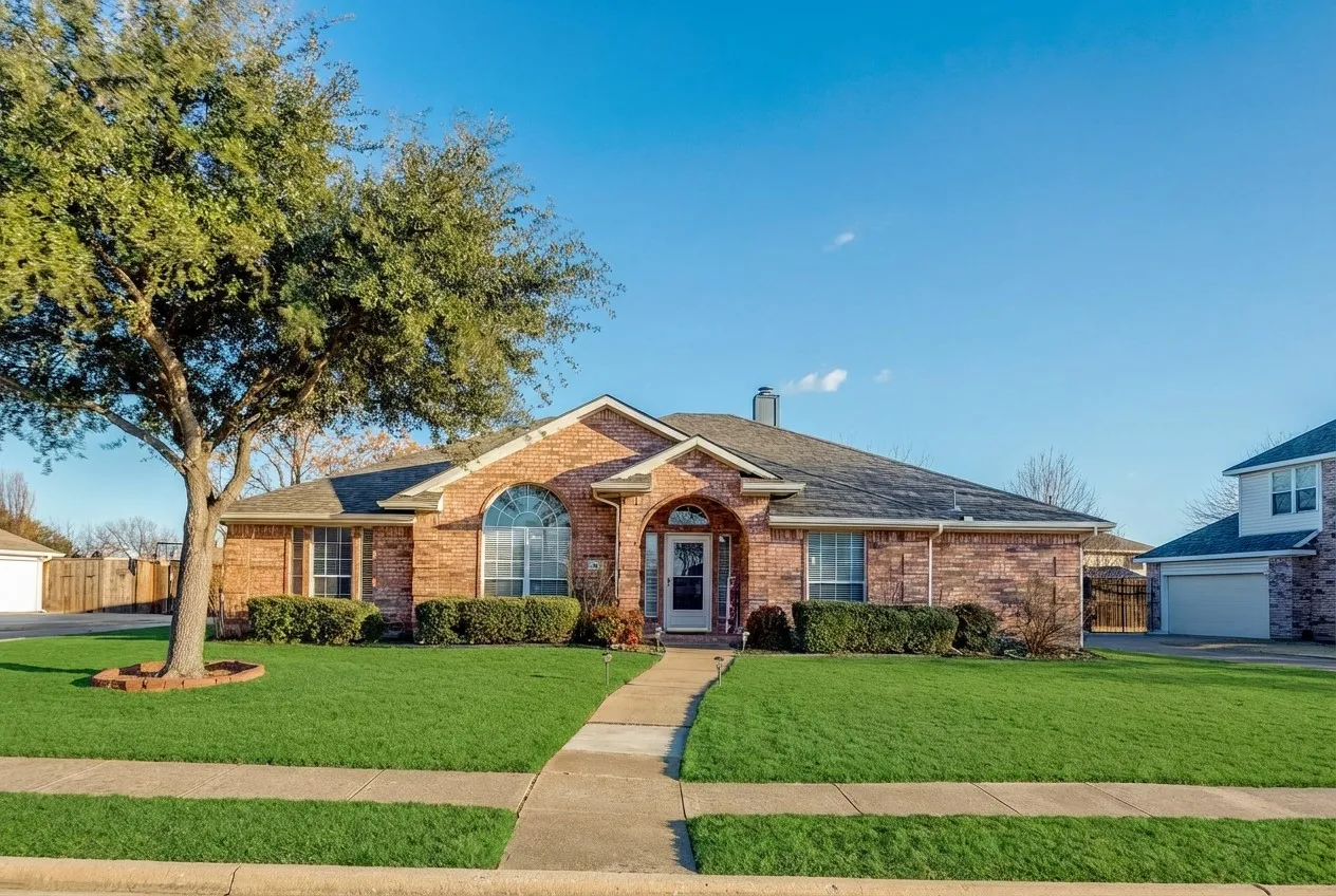 Charming brick ranch-style home featuring a manicured front lawn, stone accents, and a covered entry porch.