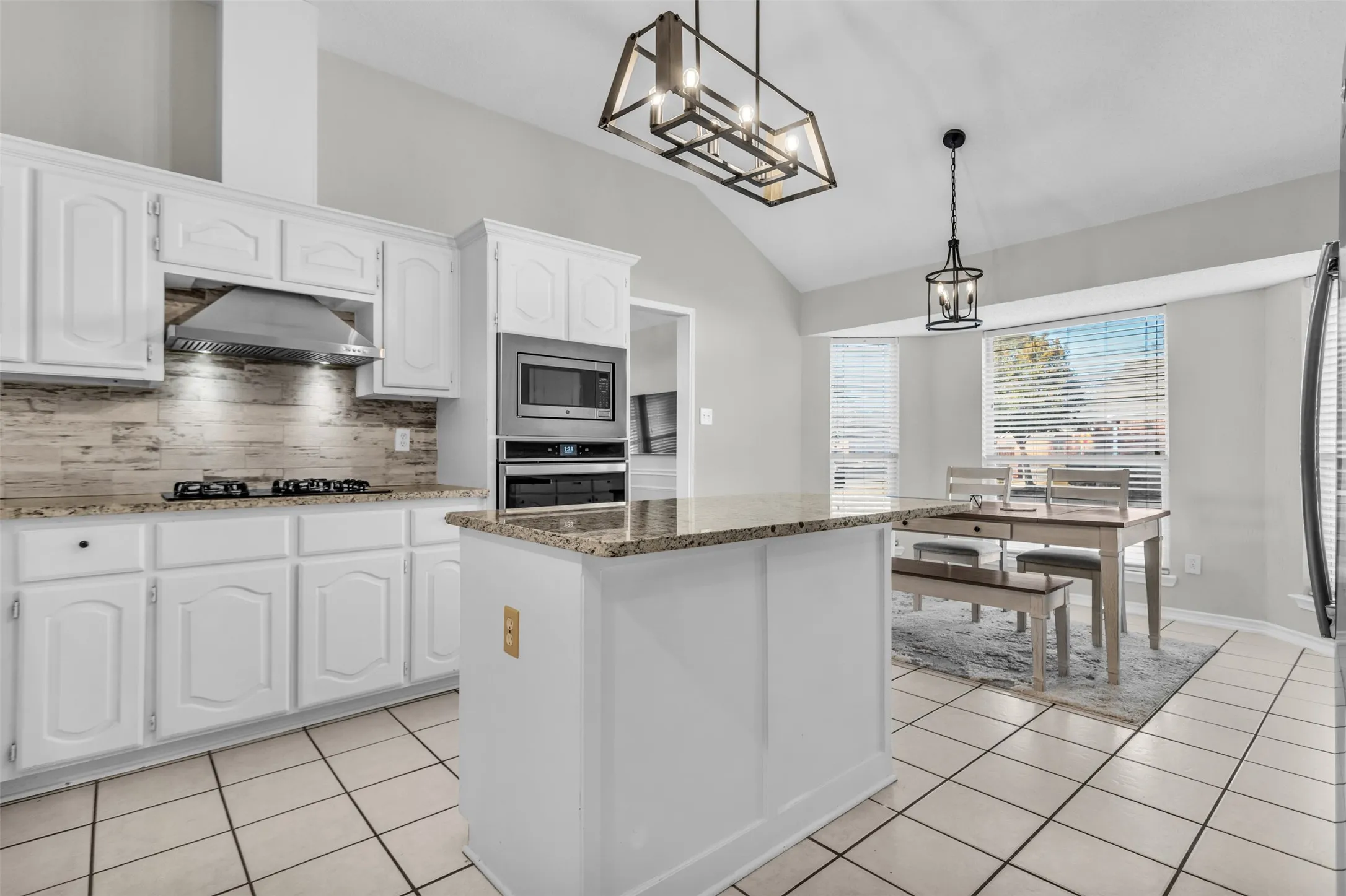 Gourmet kitchen featuring bright white cabinetry, dark stone countertops, modern pendant lighting, and stainless steel appliances.