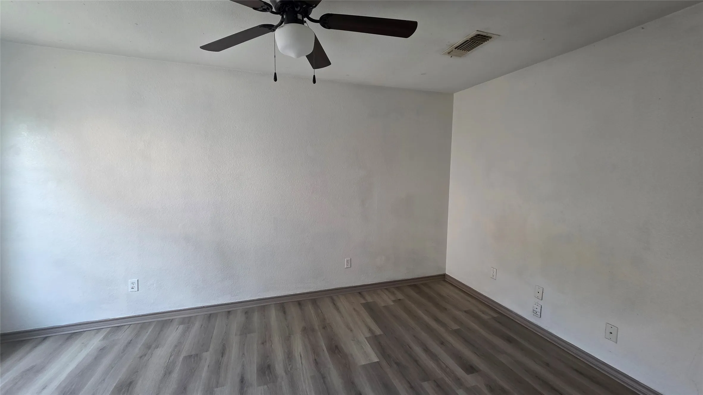 Empty room with a ceiling fan and dark wood-style floors