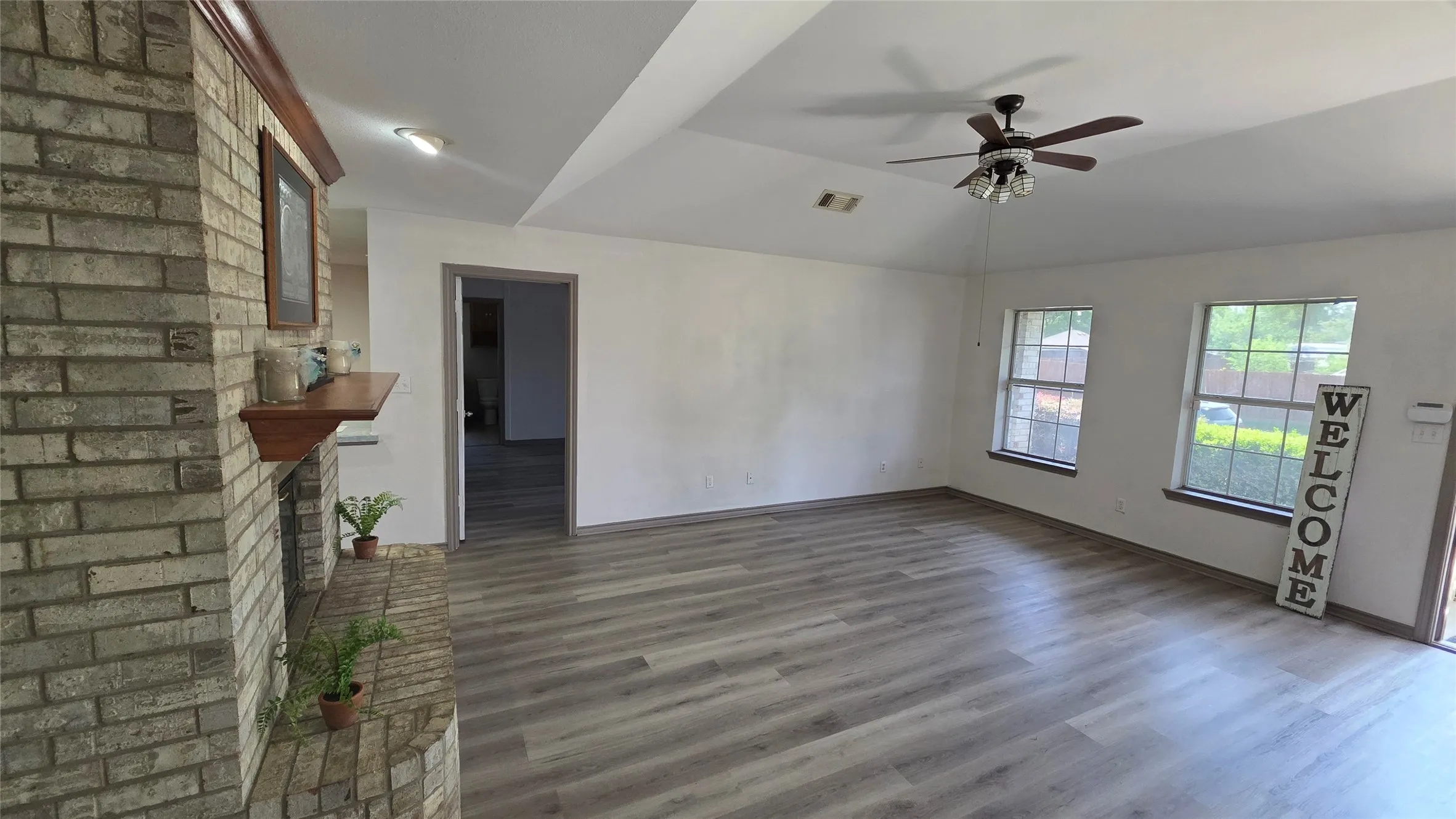 Unfurnished living room with a brick fireplace, ceiling fan, and dark wood finished floors