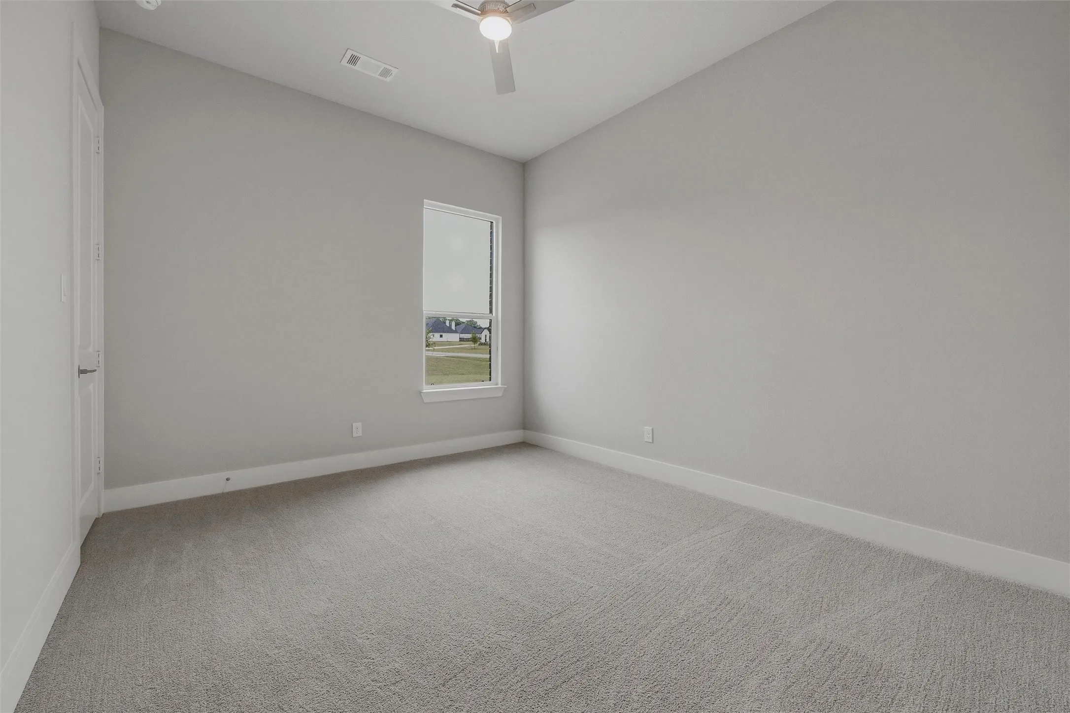 Neutral tone wall finish, plush carpet flooring, single window, white trim, and ceiling fan