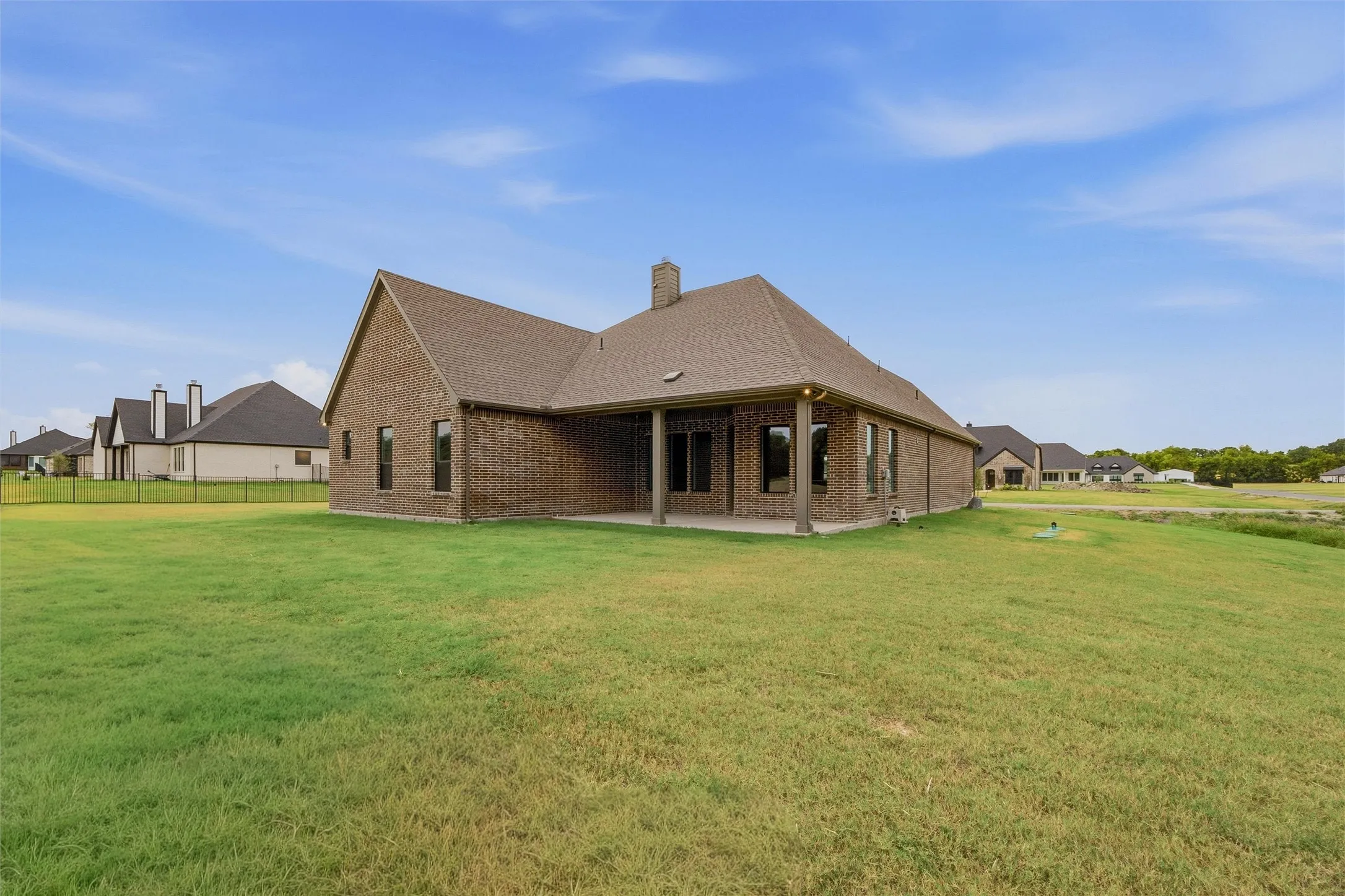 Brick exterior with a covered patio, multiple windows, and a shingled roof