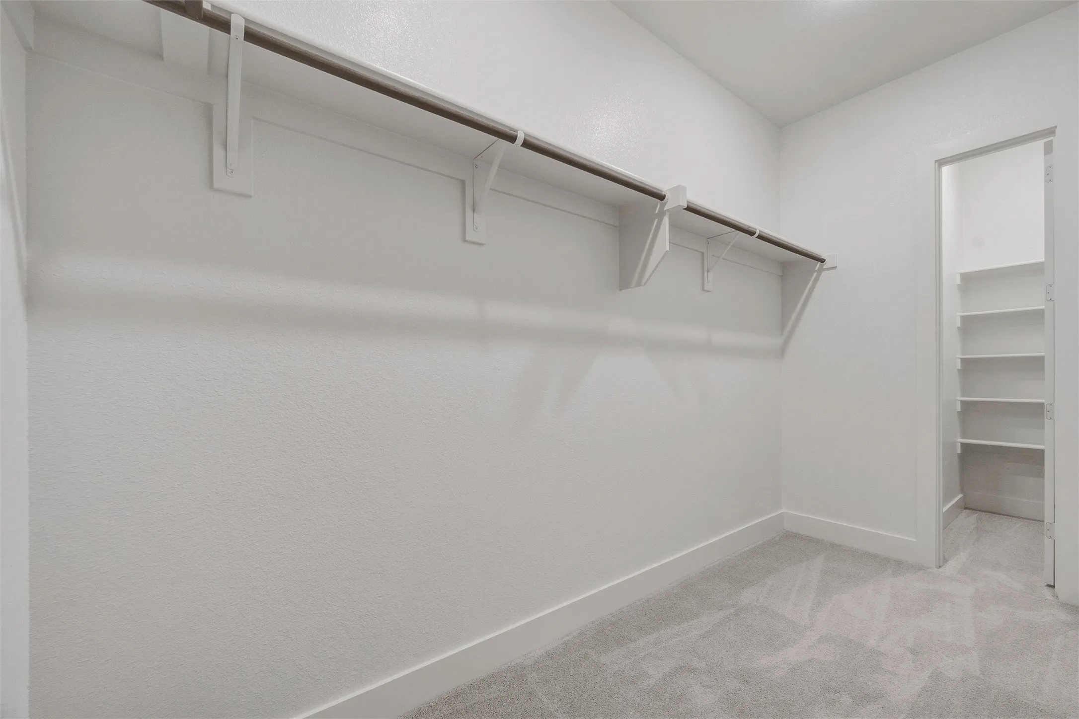 Wall-mounted closet rod with shelving, textured white walls, light gray carpet, and white trim