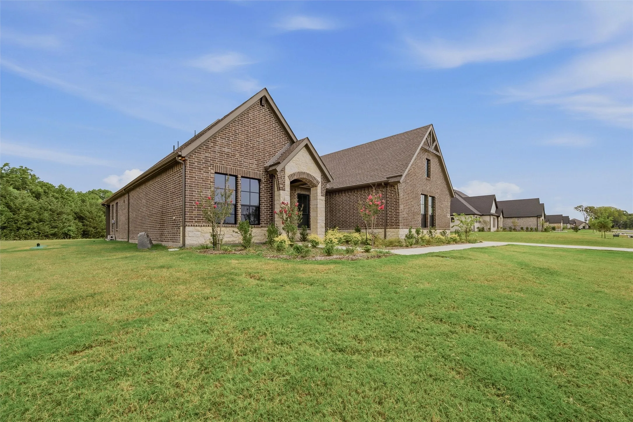 Brick exterior with stone accents, gabled rooflines, dark window frames, and a manicured lawn