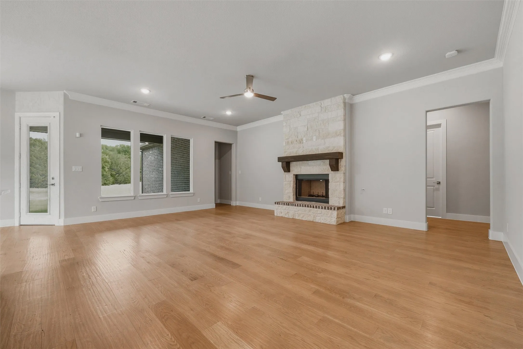 Spacious interior featuring wood-finish flooring, a stone fireplace with a wood mantle, and multiple windows